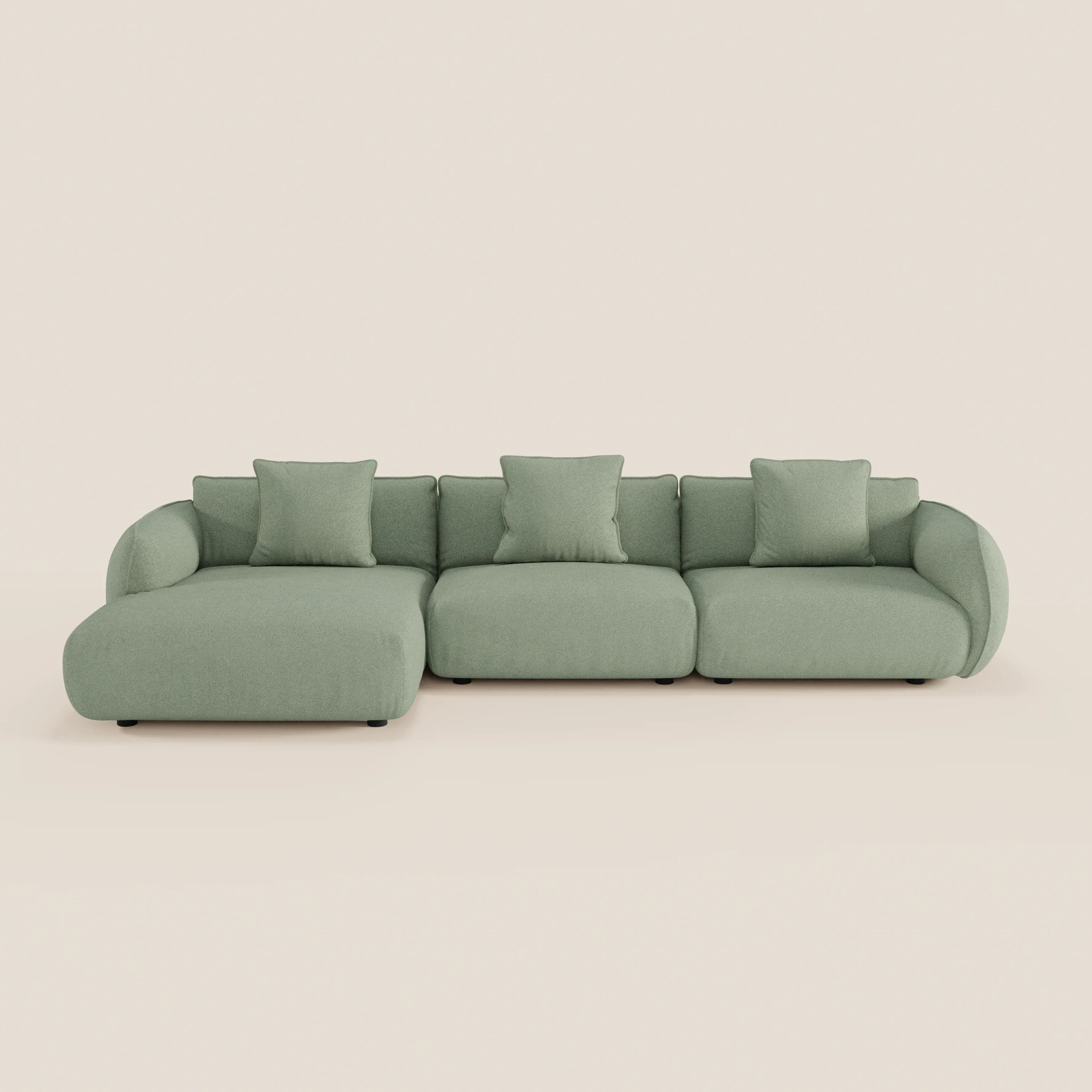 Il divano Nimbus angolare con penisola componibile di Divani.Store è un moderno componibile verde chiaro in morbido tessuto effetto cotone antimacchia, con tre sedute, braccioli bassi e curvi, quattro cuscini coordinati e una chaise lounge a sinistra su uno sfondo semplice.