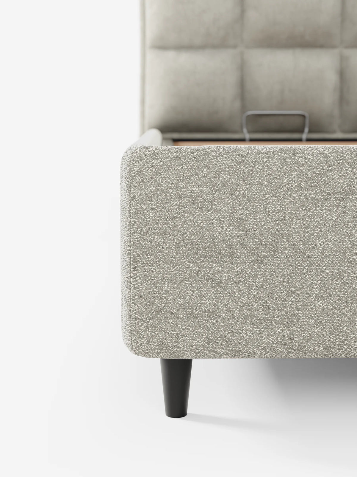 Un primo piano del letto imbottito AURO con vano contenitore e testiera alta capitonné in ciniglia Oeko-Tex® color beige chiaro, caratterizzato da una testiera alta con capitonatura quadrata, gambe corte scure e un vano contenitore aperto con struttura in legno.