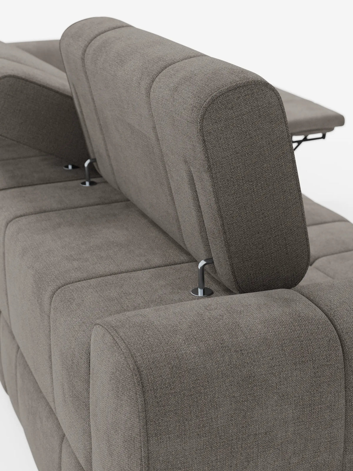 Un primo piano di un divano modulare Giotto color taupe a 4 posti con poggiatesta reclinabili e funzione relax elettrica opzionale, rivestito in tessuto smacchiabile T23, con poggiatesta regolabili su sottili supporti in metallo argentato lucido su uno sfondo chiaro.
