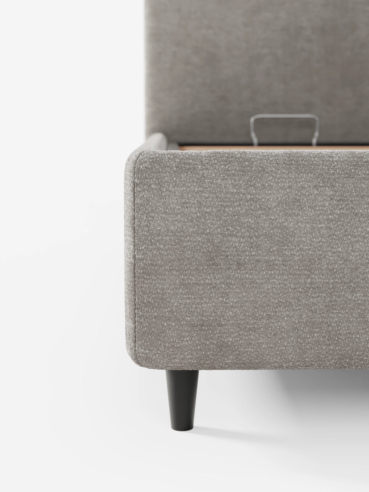 Primo piano dell'angolo di un divano KAELOS “letto minimal” imbottito color taupe con finitura testurizzata - vano contenitore, piedini alti e testiera arrotondata in tessuto ciniglia, caratterizzato da una gamba nera affusolata e da una maniglia in metallo per il vano contenitore ribaltabile.