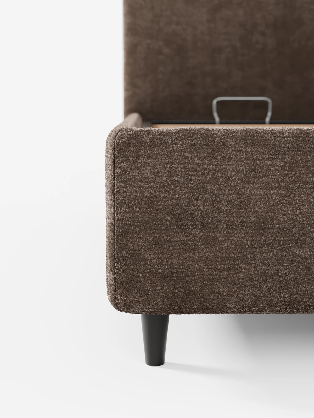Un letto KAELOS minimal imbottito color marrone - con vano contenitore, piedini alti e testiera arrotondata in tessuto ciniglia con finitura testurizzata - poggia su gambe nere corte e affusolate, parzialmente aperte per rivelare il vano contenitore interno.