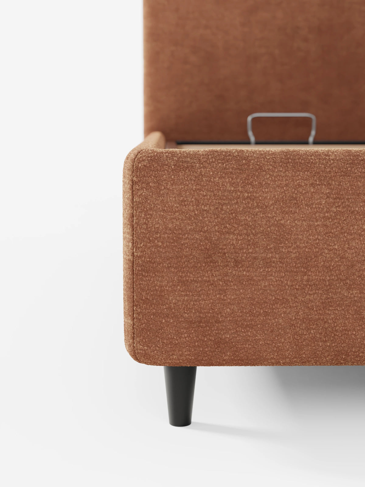 Un primo piano di un letto KAELOS minimal imbottito color ruggine con finitura testurizzata, caratterizzato da una testiera arrotondata, una base rialzata con vano contenitore e una sottile gamba nera su uno sfondo bianco a tinta unita.