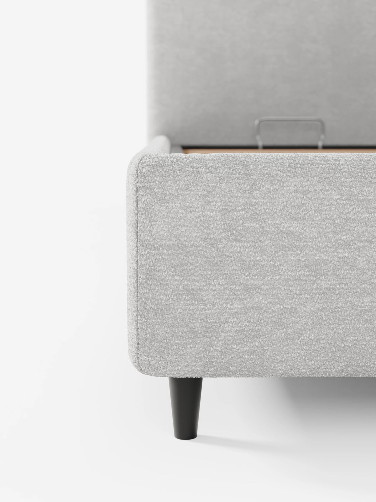 Un primo piano di un divano KAELOS “letto minimal” imbottito, color grigio chiaro, con vano contenitore, piedini alti e testiera arrotondata in tessuto ciniglia dalla trama rigata, testiera alta e arrotondata e base rialzata che rivela un vano contenitore.