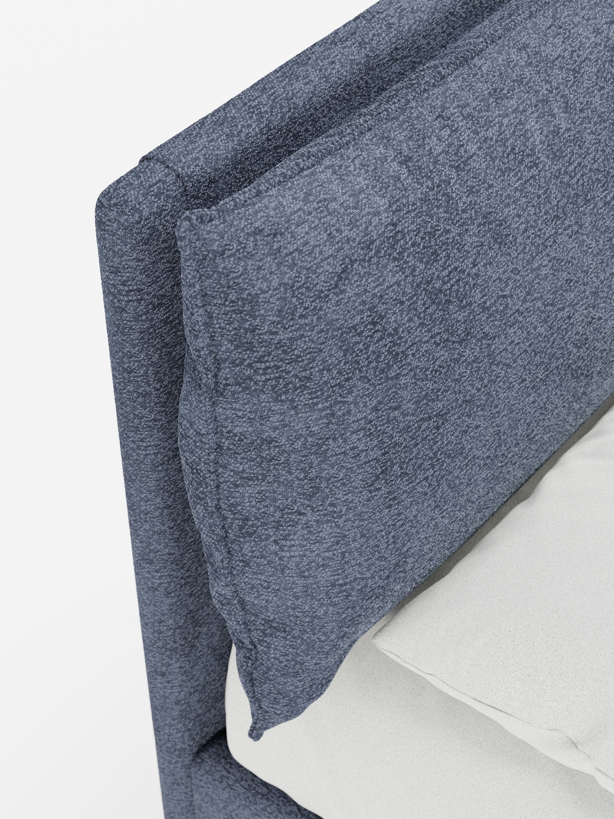 Primo piano dell’angolo superiore del letto imbottito ZAYRON con contenitore e morbidi cuscini regolabili di Letti.store, caratterizzato da una testiera in tessuto blu-grigio testurizzato certificato Oeko-Tex® con una sezione imbottita e soffice. È visibile una parte del materasso bianco e del lenzuolo, che accentua il contrasto tra i materiali morbidi e le linee moderne e pulite del letto.