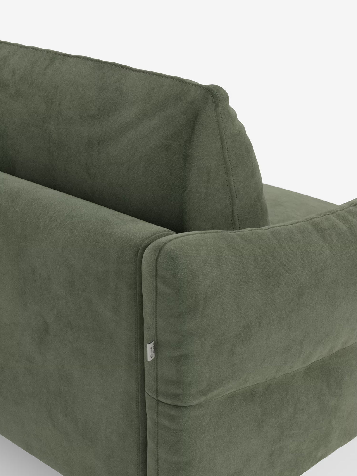 Un primo piano dello schienale e del bracciolo del divano letto Dalia a 2, 3 e 4 posti con materasso H18 di Divani.Store, rivestito in moderno tessuto di velluto T30 resistente alle macchie. Il divano presenta cuscini morbidi e una trama liscia, con una piccola etichetta in tessuto bianco cucita sulla cucitura del bracciolo. Lo sfondo è bianco a tinta unita.