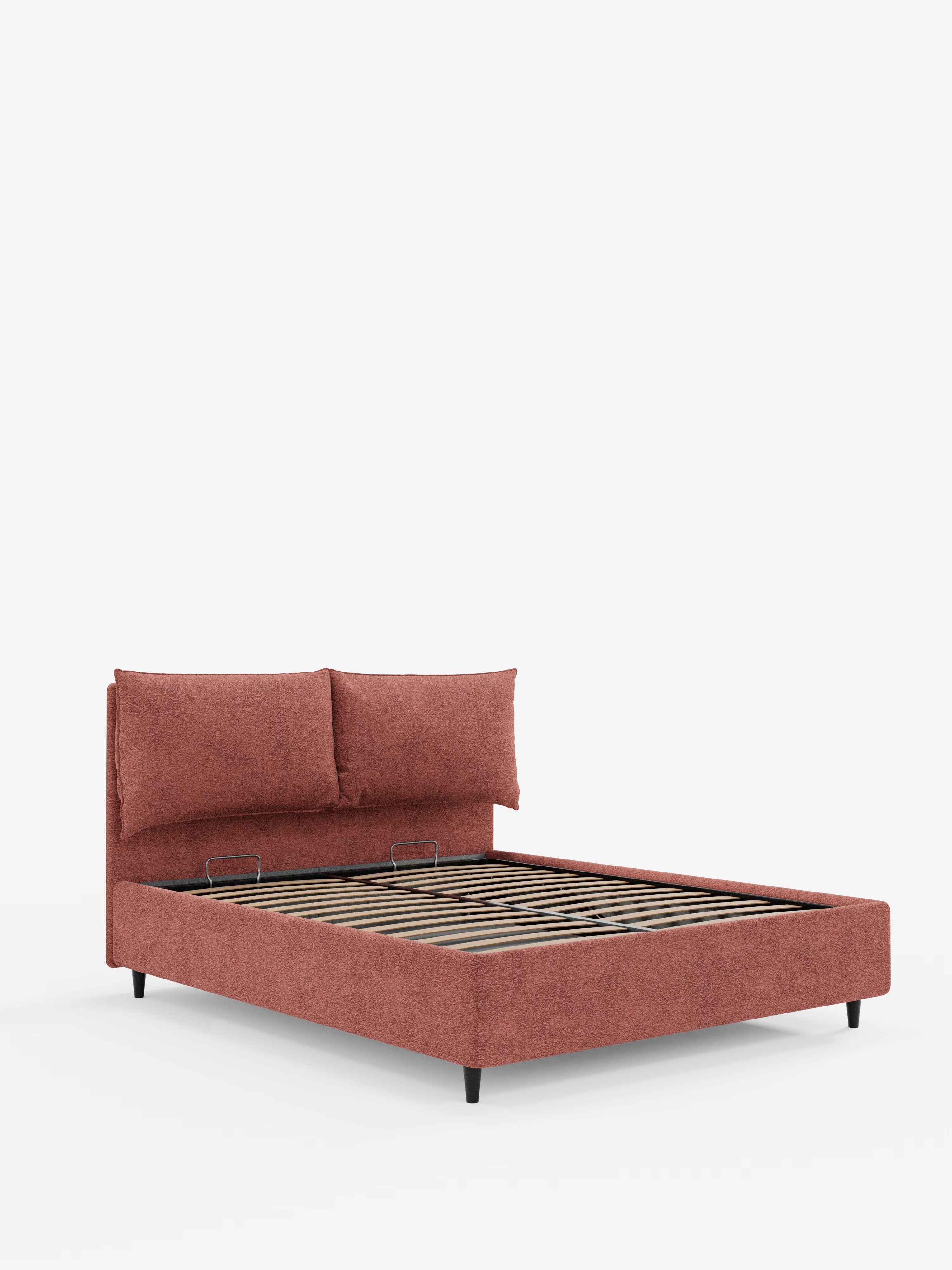 Un letto imbottito ZAYRON dal design contemporaneo di Letti., caratterizzato da una testiera e una base rivestite in tessuto color ruggine certificato Oeko-Tex®, con due morbidi cuscini regolabili per la testiera, robuste doghe in legno per il sostegno del materasso, un pratico vano contenitore e gambe corte nere, il tutto in risalto su uno sfondo bianco a tinta unita.