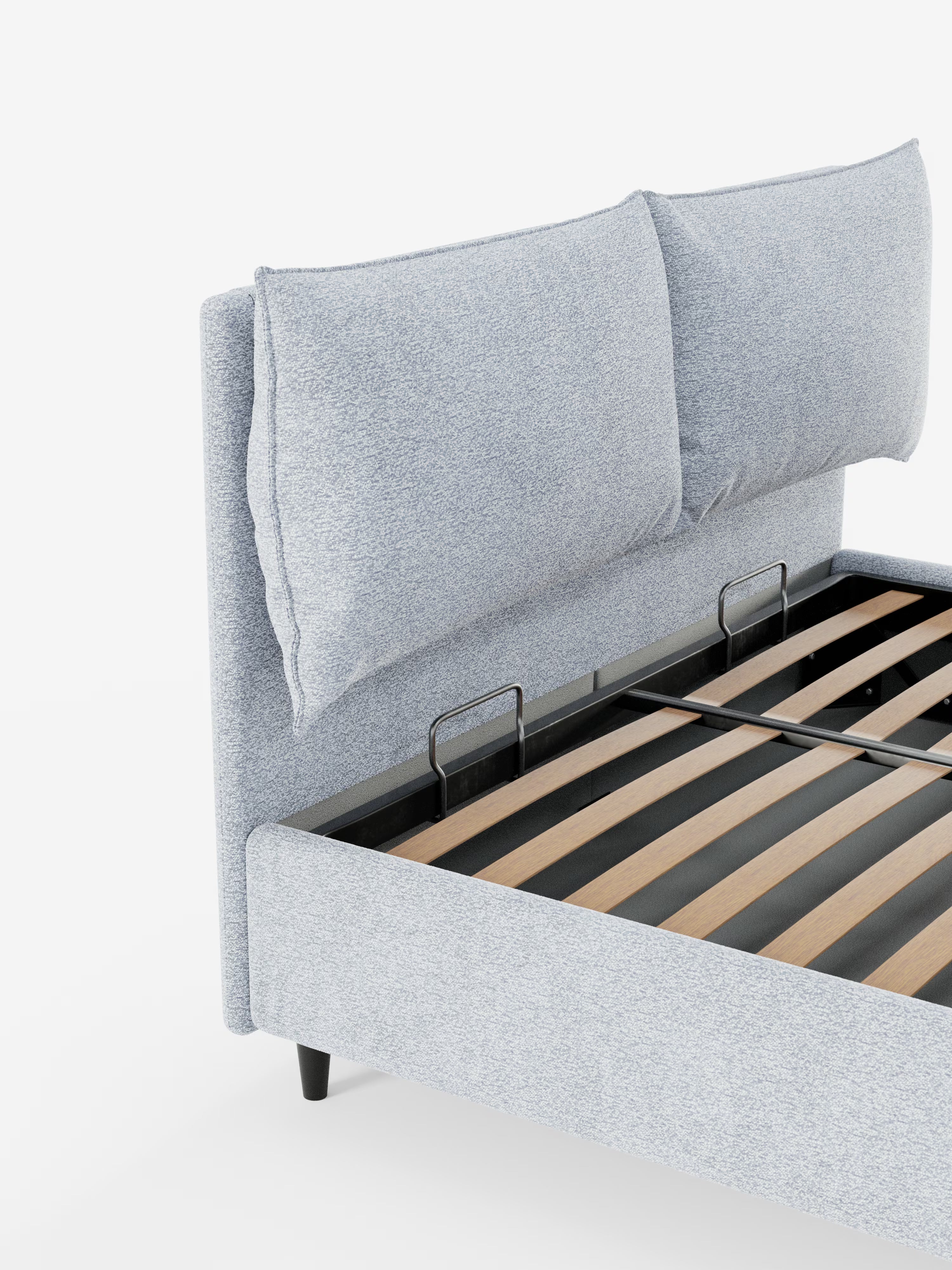 Su uno sfondo bianco è raffigurata una vista parziale del letto imbottito ZAYRON con contenitore e morbidi cuscini regolabili di Letti.store. Questo letto moderno presenta una testiera in tessuto grigio chiaro certificato Oeko-Tex® con due grandi e morbidi cuscini regolabili, completata da doghe in legno a vista e supporti in metallo nero.