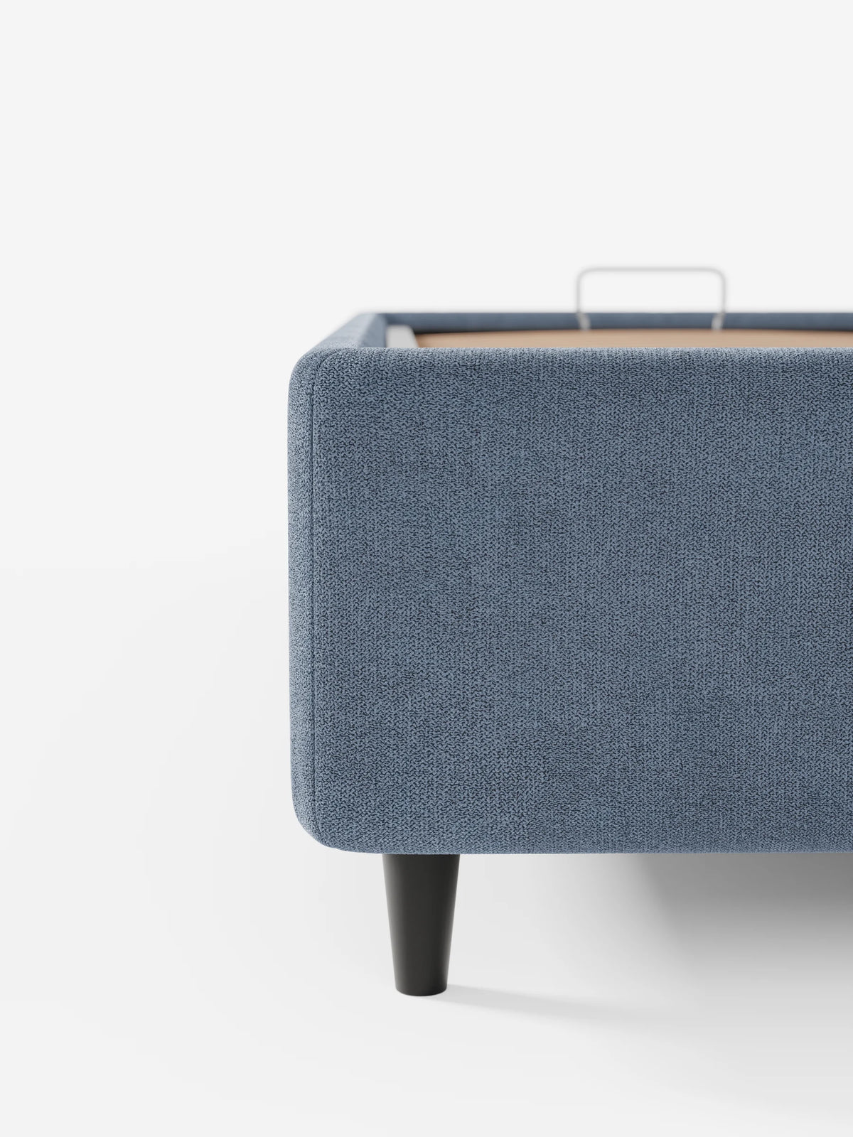 Un primo piano di un letto sommier blu ERON imbottito con vano contenitore in tessuto impermeabile certificato Oeko-Tex, caratterizzato da angoli arrotondati e gambe affusolate di colore scuro, che mostra l'interno del vano contenitore e la maniglia in metallo.