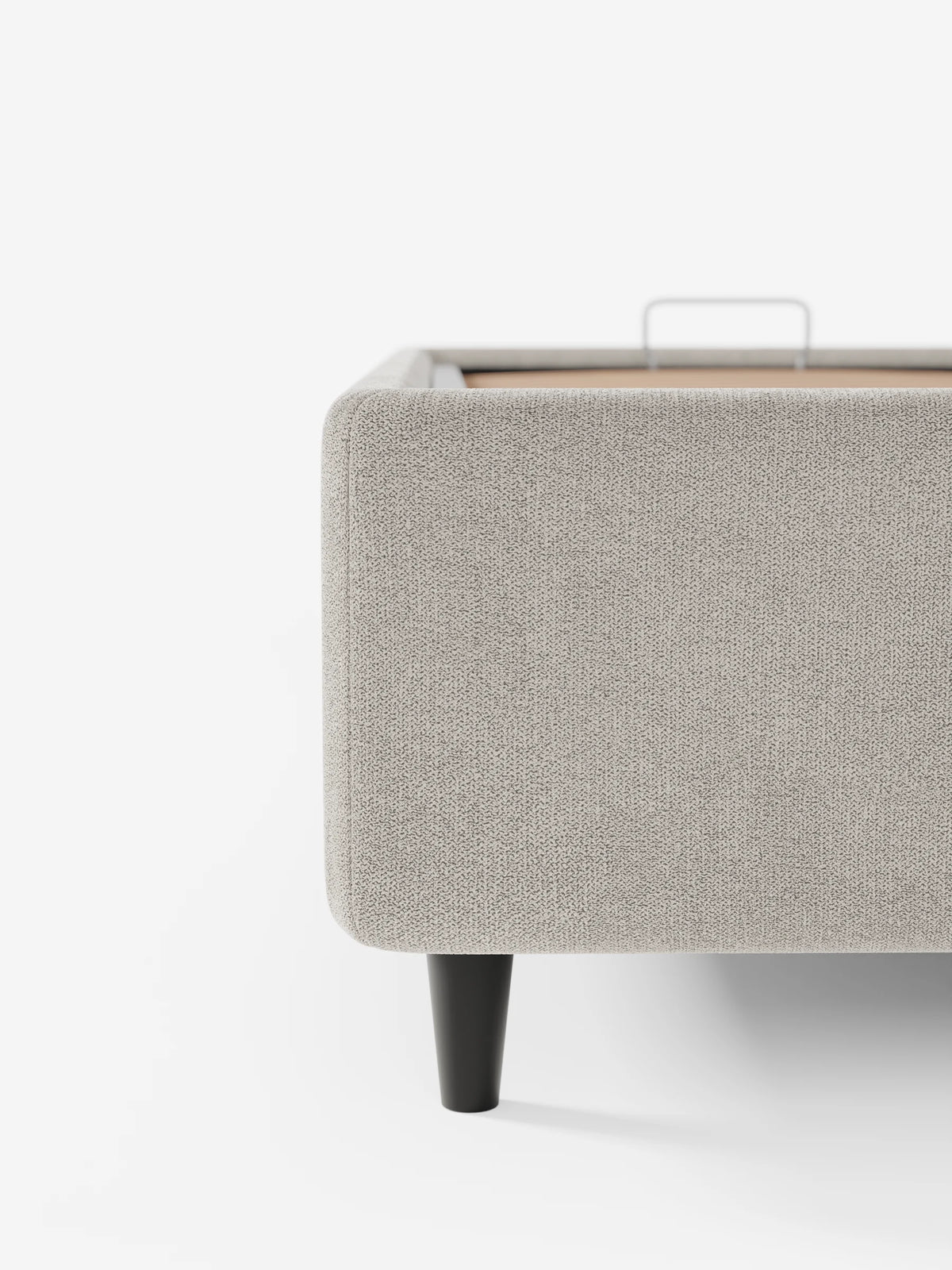 Un primo piano di un letto sommier ERON grigio chiaro, imbottito e dotato di vano contenitore in tessuto impermeabile certificato Oeko-Tex. La struttura imbottita poggia su una gamba corta e conica di colore scuro, che lascia intravedere una maniglia in metallo sulla piattaforma interna.