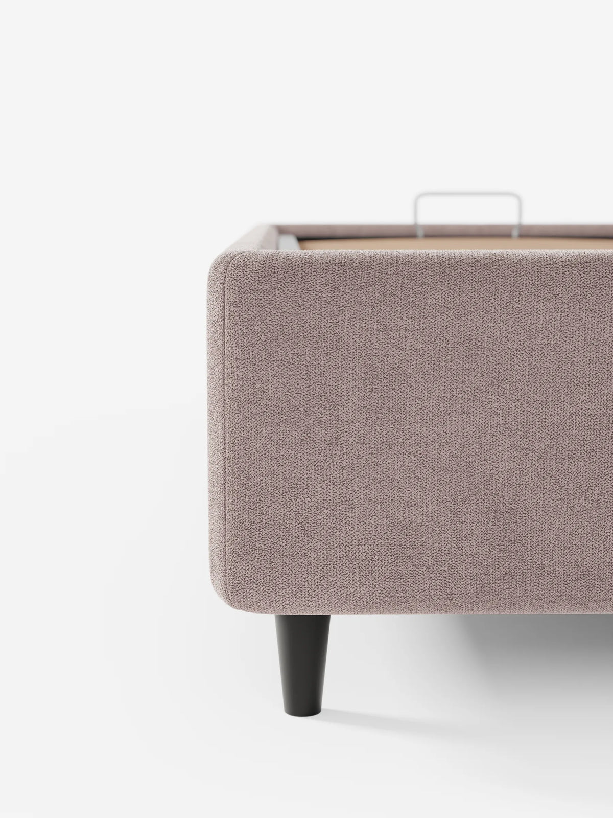 Un primo piano del letto sommier imbottito ERON, di colore grigio-malva, con vano contenitore in tessuto impermeabile certificato Oeko-Tex, caratterizzato da una gamba affusolata scura e da una maniglia in metallo sul bordo interno del vano contenitore.