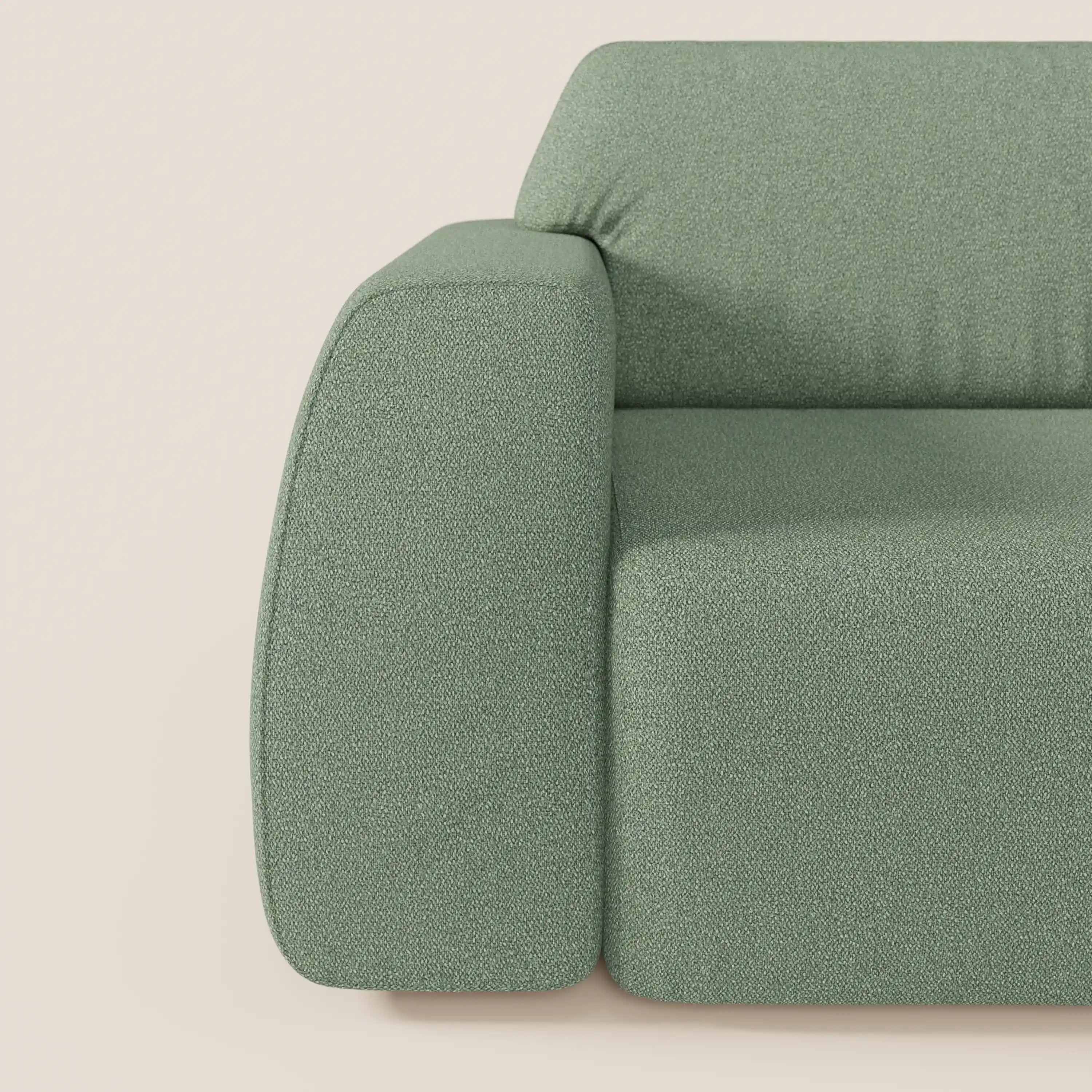 Primo piano del lato sinistro del divano Orbit con 3 sedute scorrevoli e allungabili in tessuto effetto cotone smacchiabile T33 di Divani.Store, di colore verde salvia con imbottitura testurizzata e bracciolo arrotondato, su sfondo crema chiaro.