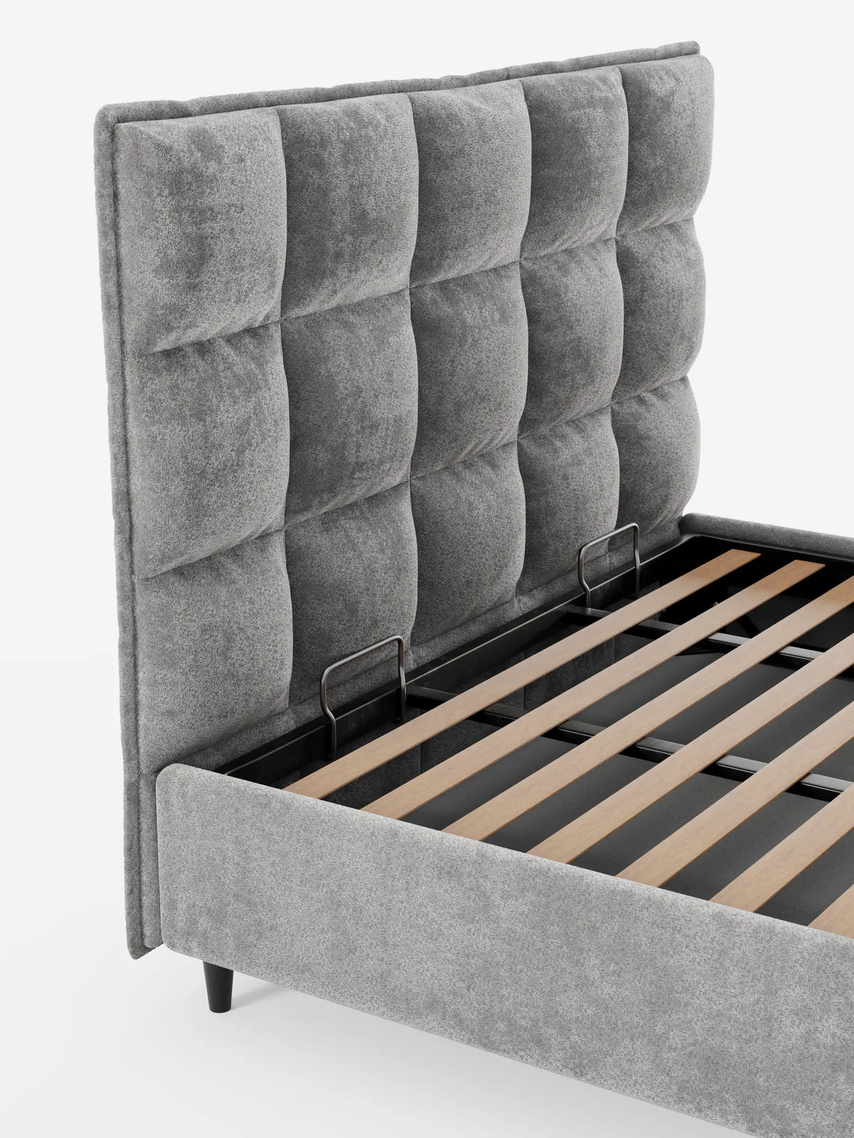 AURO, letto imbottito con contenitore e testiera alta capitonné in ciniglia Oeko-Tex®, caratterizzato da una testiera alta, grigia e con trapuntatura a quadrati. La struttura è parzialmente aperta, lasciando intravedere le doghe in legno che sostengono un vano contenitore profondo su uno sfondo bianco.