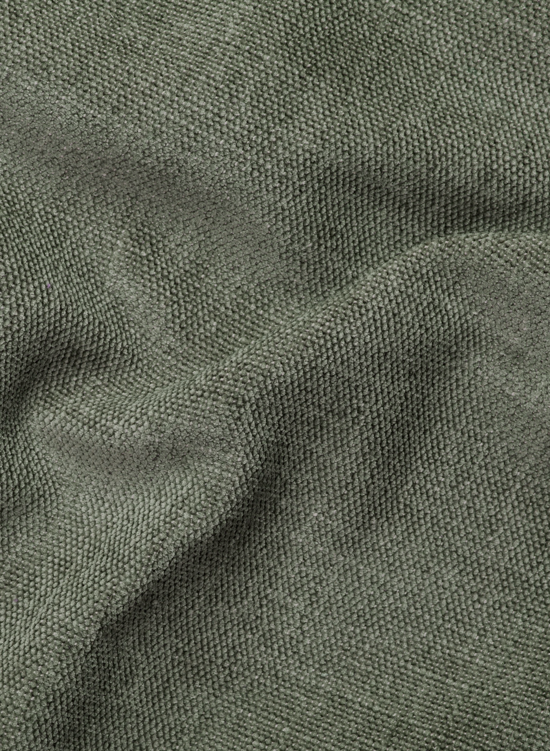 Un primo piano del tessuto verde oliva del divano Ischia a 3 posti con pouf estraibile e schienali traslanti in tessuto misto lino smacchiabile, caratterizzato da una trama a rilievo e da morbide pieghe che creano delicate ombre.