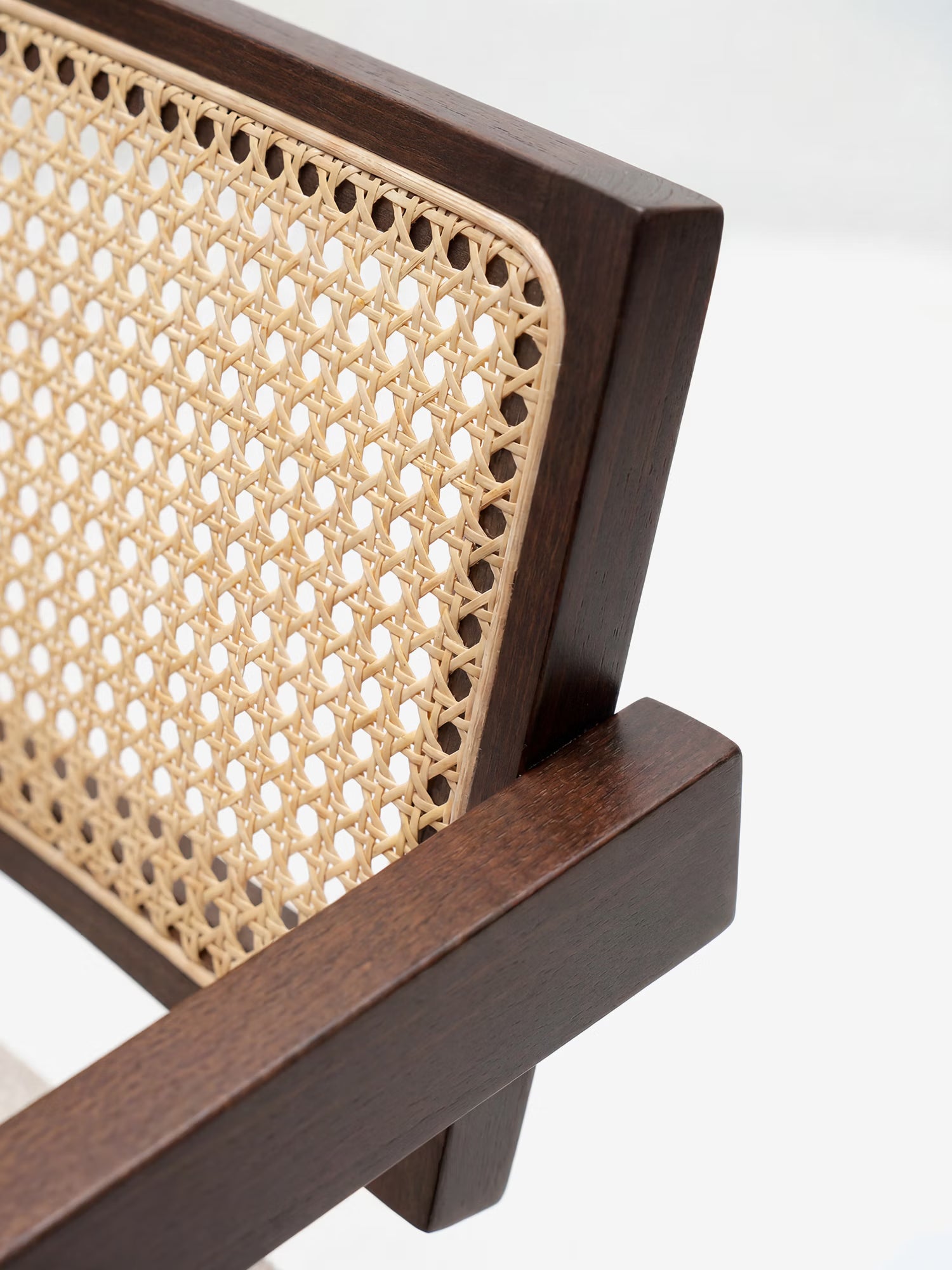 Primo piano della sedia Antea con braccioli di Divani.Store, realizzata in legno massello di wengé, caratterizzata da uno schienale in rattan intrecciato con motivi geometrici e da una seduta imbottita in misto cotone che esaltano il contrasto di texture e colori.