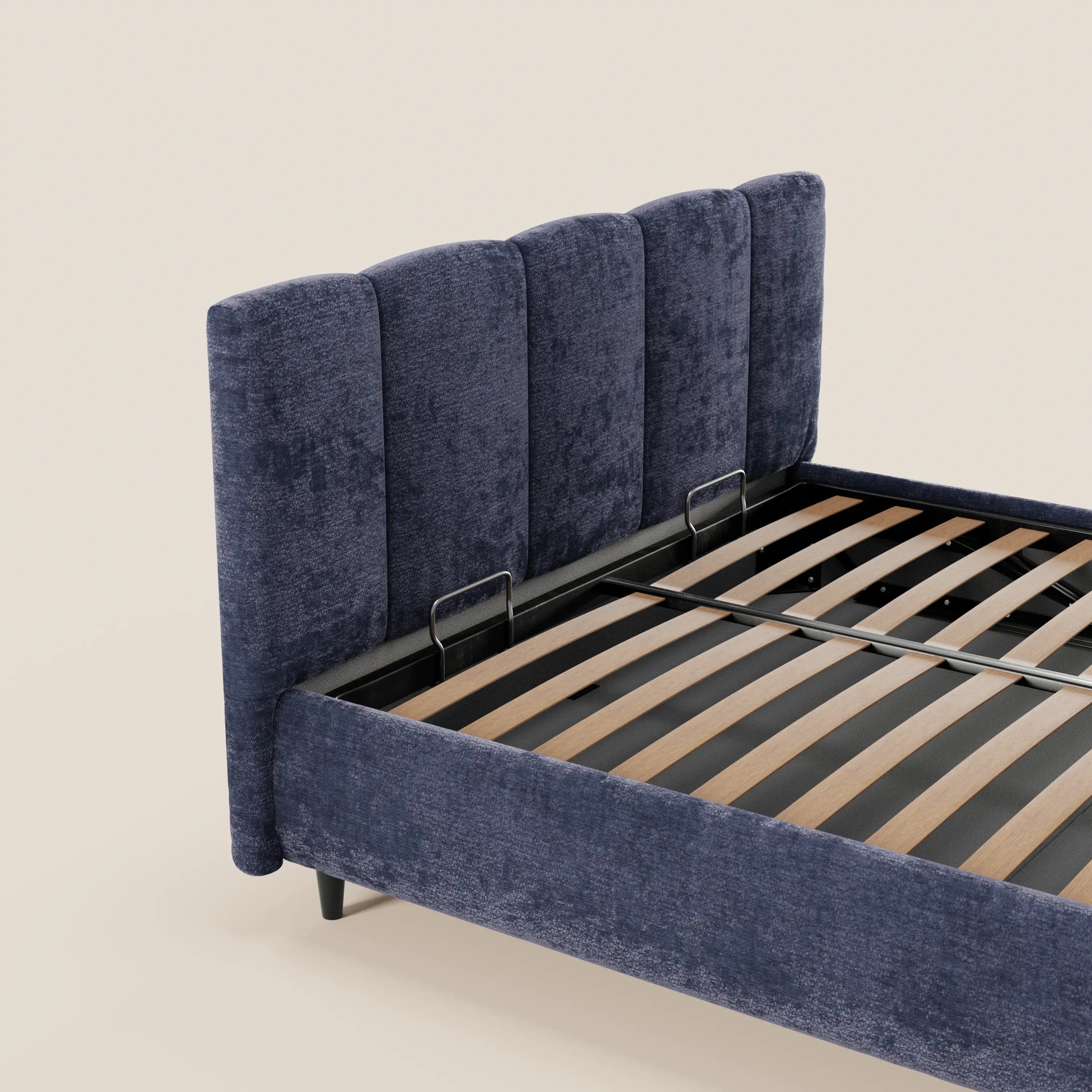 Il letto imbottito ARKAM di Letti.store presenta una testiera verticale in tessuto Oeko-Tex®, un vano contenitore e un design shabby chic. Immagine che lo ritrae parzialmente su sfondo beige, con doghe in legno e supporti neri a vista, visto di profilo.