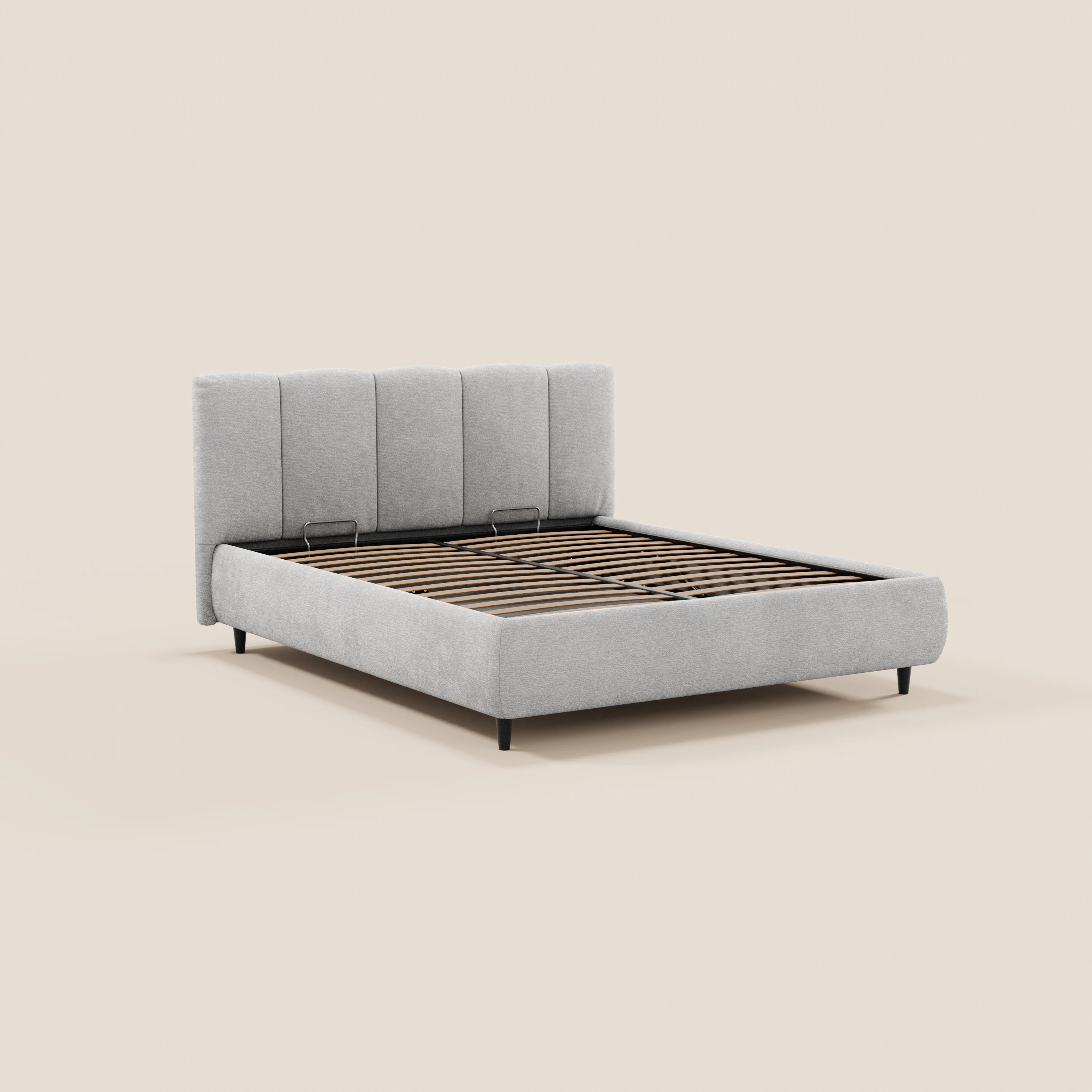 Il letto imbottito ARKAM di Letti.store presenta una testiera alta con cuciture verticali e una base contenitore, realizzata in tessuto certificato Oeko-Tex®. Nella foto è raffigurato in grigio chiaro con gambe nere e doghe in legno a vista, su uno sfondo beige. Stile shabby chic.
