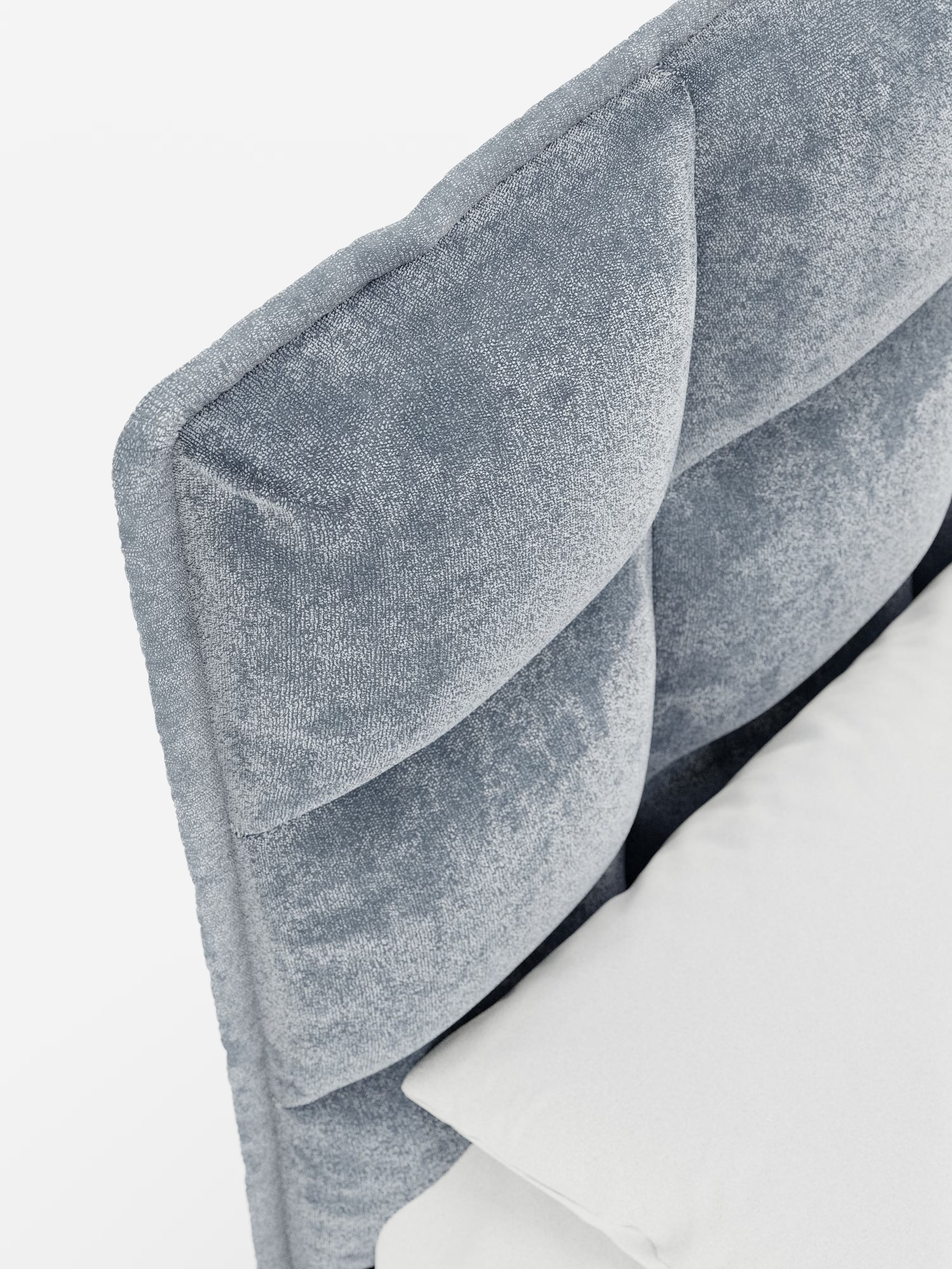 Primo piano del letto imbottito AURO con contenitore e testiera alta capitonné in ciniglia Oeko-Tex® di Letti.store, che mette in risalto la sua testiera alta capitonné rivestita in morbida ciniglia azzurra dalla trama ricca. Le ampie e morbide sezioni rettangolari esaltano l’estetica moderna, in contrasto con il cuscino e le lenzuola di un bianco candido. Lo sfondo bianco a tinta unita mette in risalto i materiali pregiati e la maestria artigianale del letto.