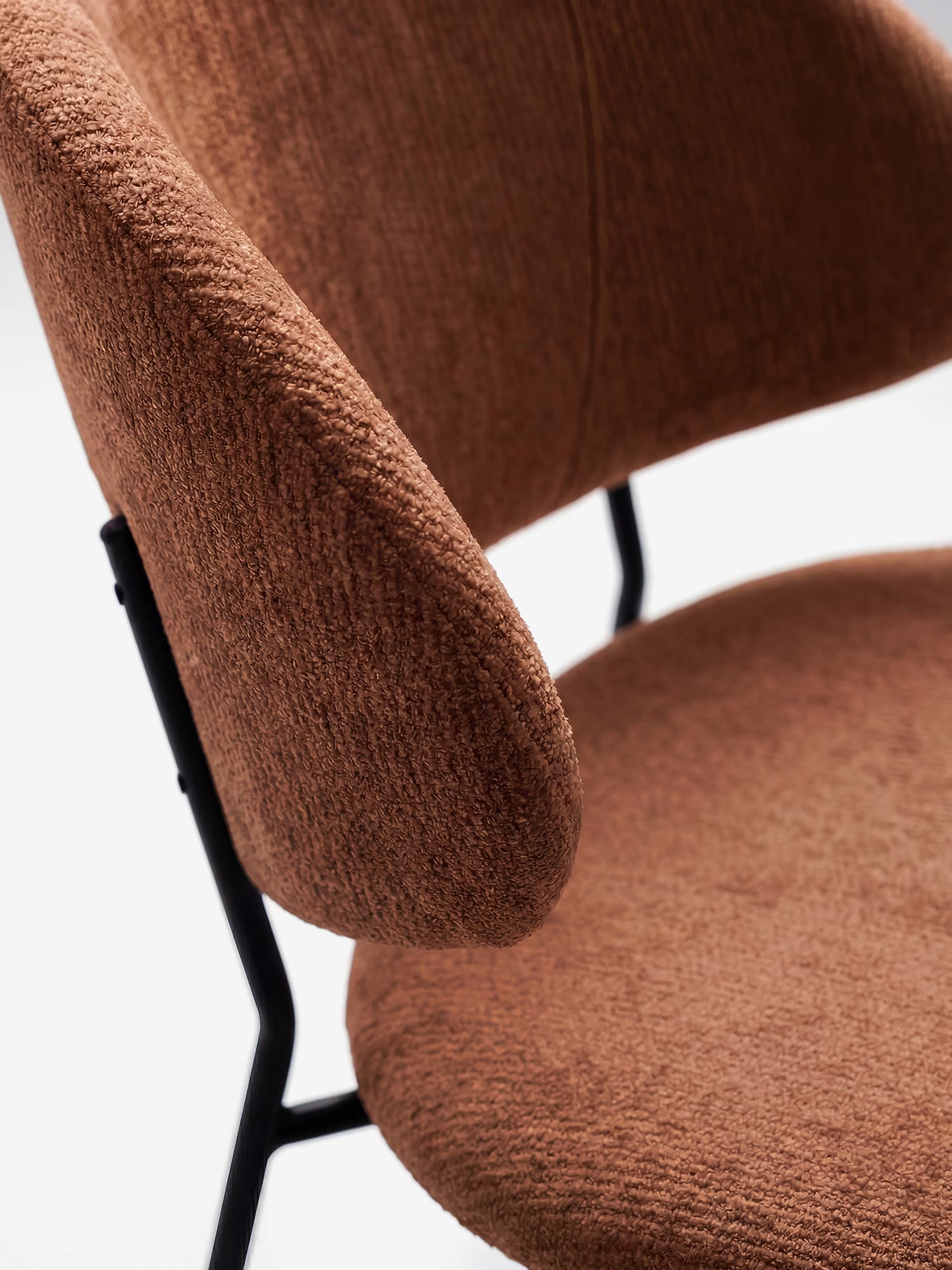 Primo piano della sedia Bruma di Divani.Store, realizzata in elegante tessuto goffrato marrone, con schienale avvolgente, braccioli e gambe in metallo nero: un esempio di design minimalista su sfondo bianco.