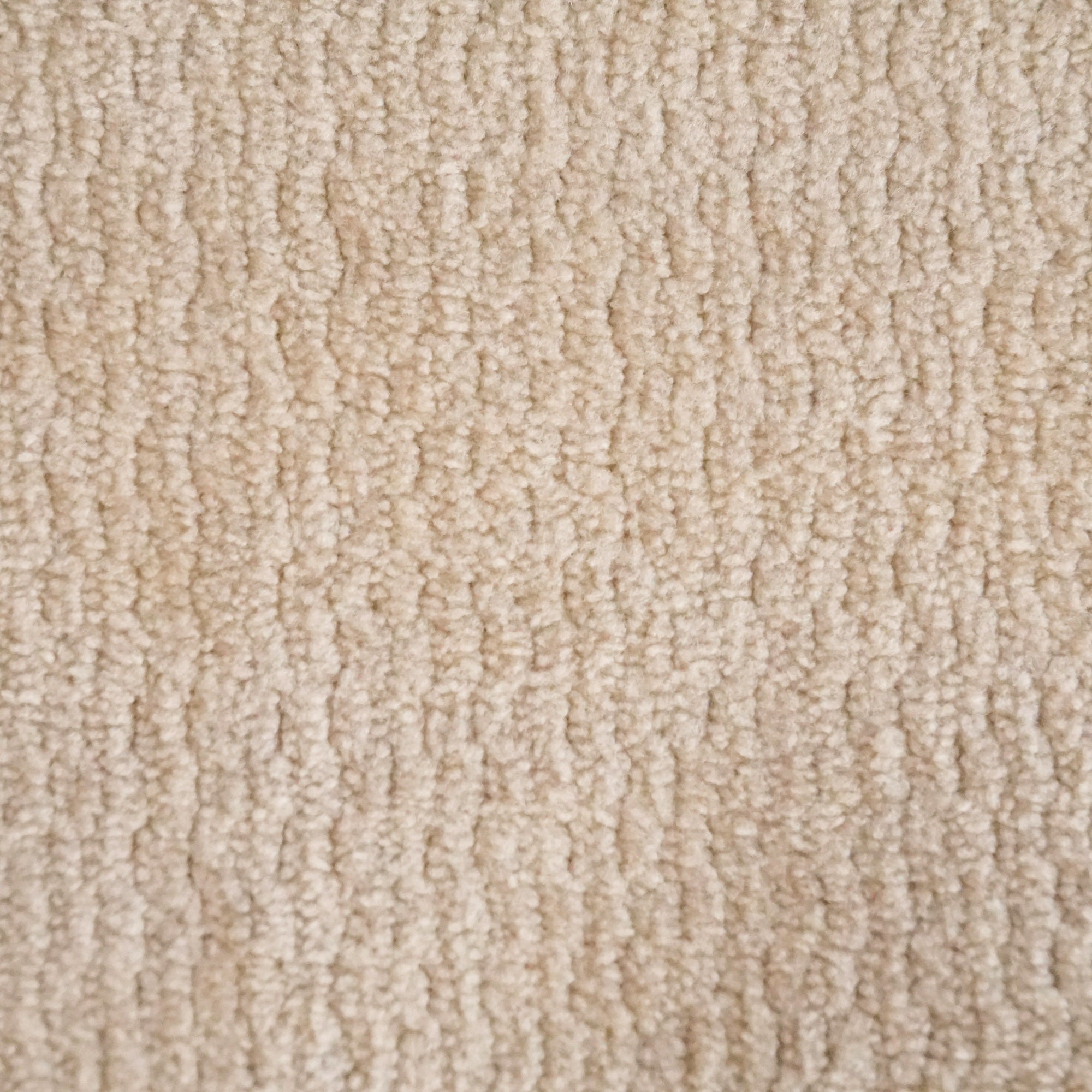 Primo piano del tessuto morbido T32 Kendal di Divani.Store, caratterizzato da una superficie morbida e fittamente intrecciata con un sottile motivo ondulato. Il tessuto beige è impermeabile e antimacchia e offre una sensazione di calore e accoglienza senza oggetti o segni visibili.