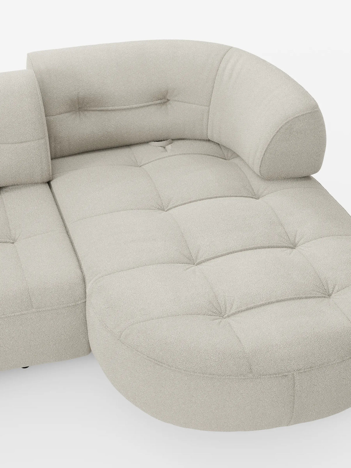 Un divano angolare Croissant color beige, dal design a forma di fagiolo e con schienali scorrevoli, rivestito in morbido tessuto effetto cotone smacchiabile T33, caratterizzato da un motivo a griglia trapuntato, bordi arrotondati e uno schienale curvo su uno sfondo bianco sporco.