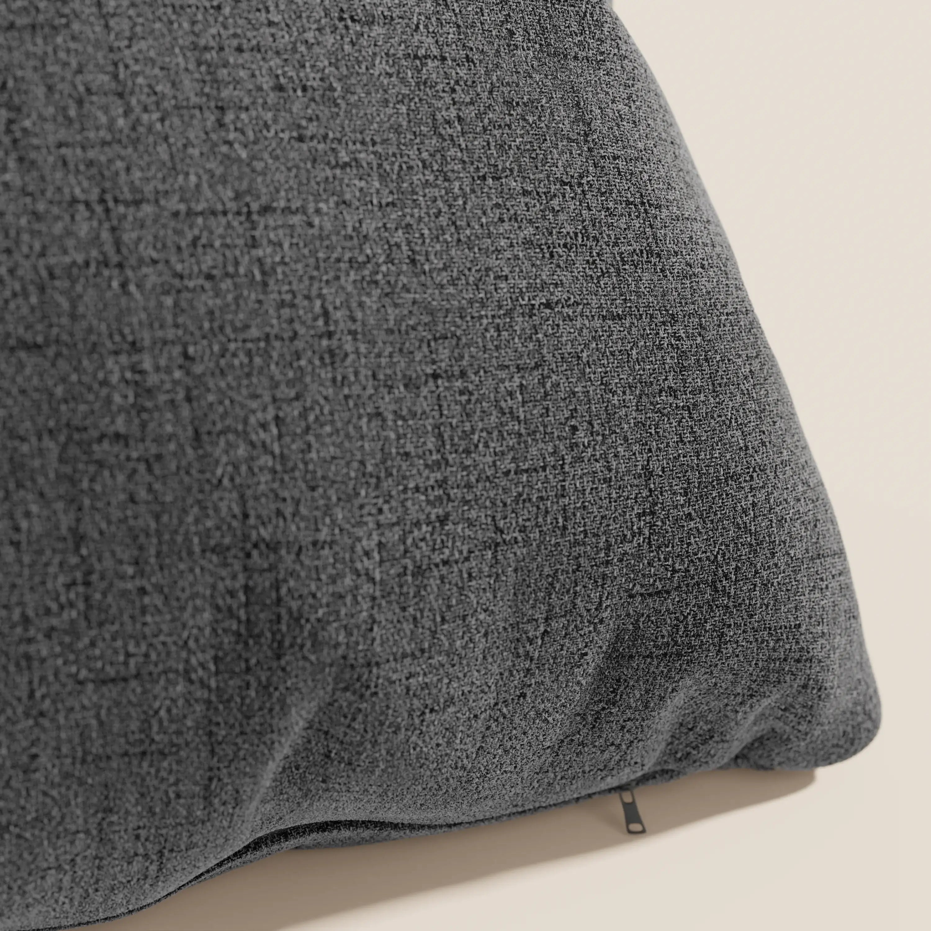 Un primo piano del cuscino Felis di Divani.Store in T03 antracite, realizzato in morbido tessuto idrorepellente, mostra il sottile motivo a griglia intrecciata e la cerniera parzialmente visibile su uno sfondo beige chiaro.