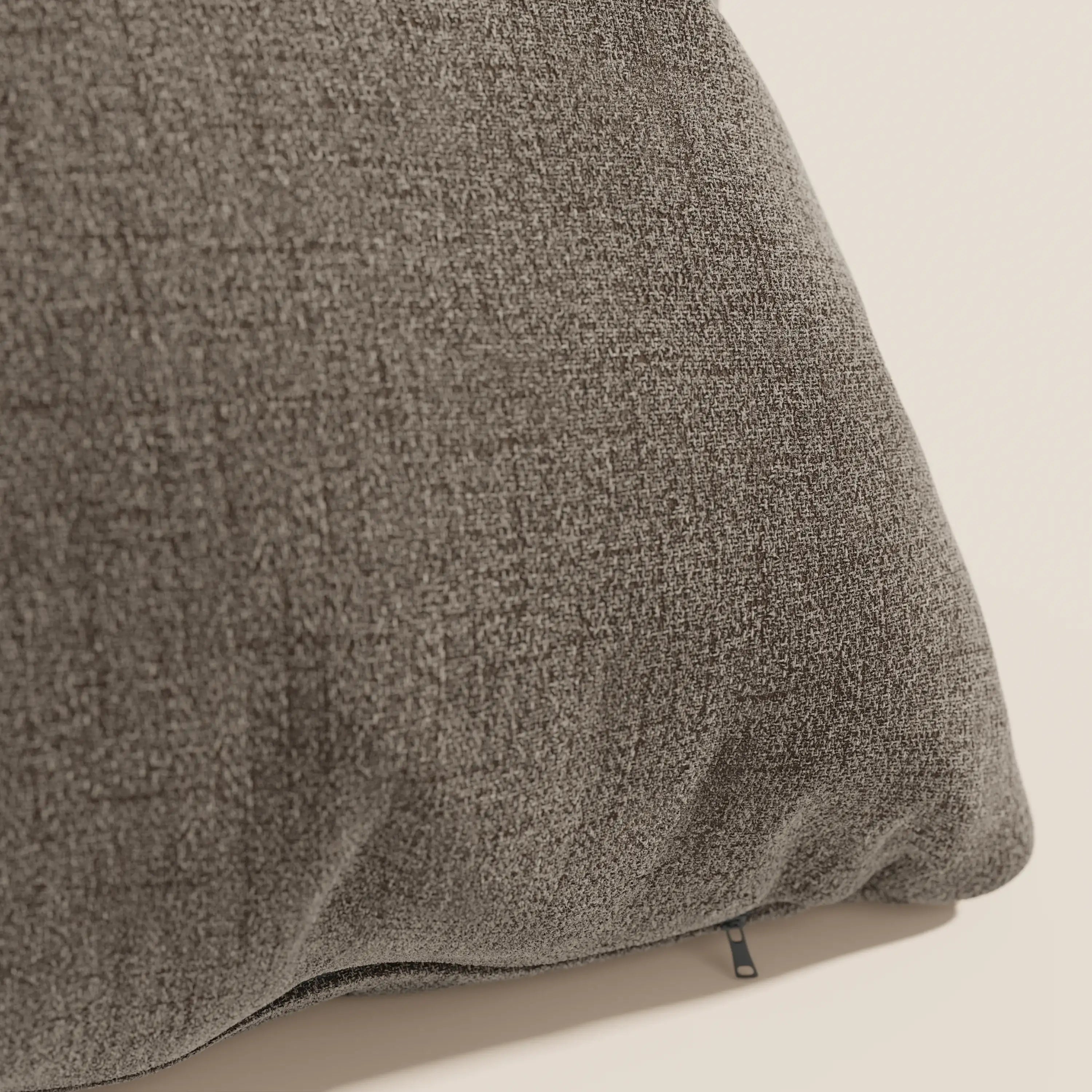 Primo piano del cuscino Felis di Divani.Store in morbido tessuto impermeabile T03 marrone, caratterizzato da una trama intrecciata e da una cerniera a vista, perfetto per un uso decorativo su sfondi neutri.
