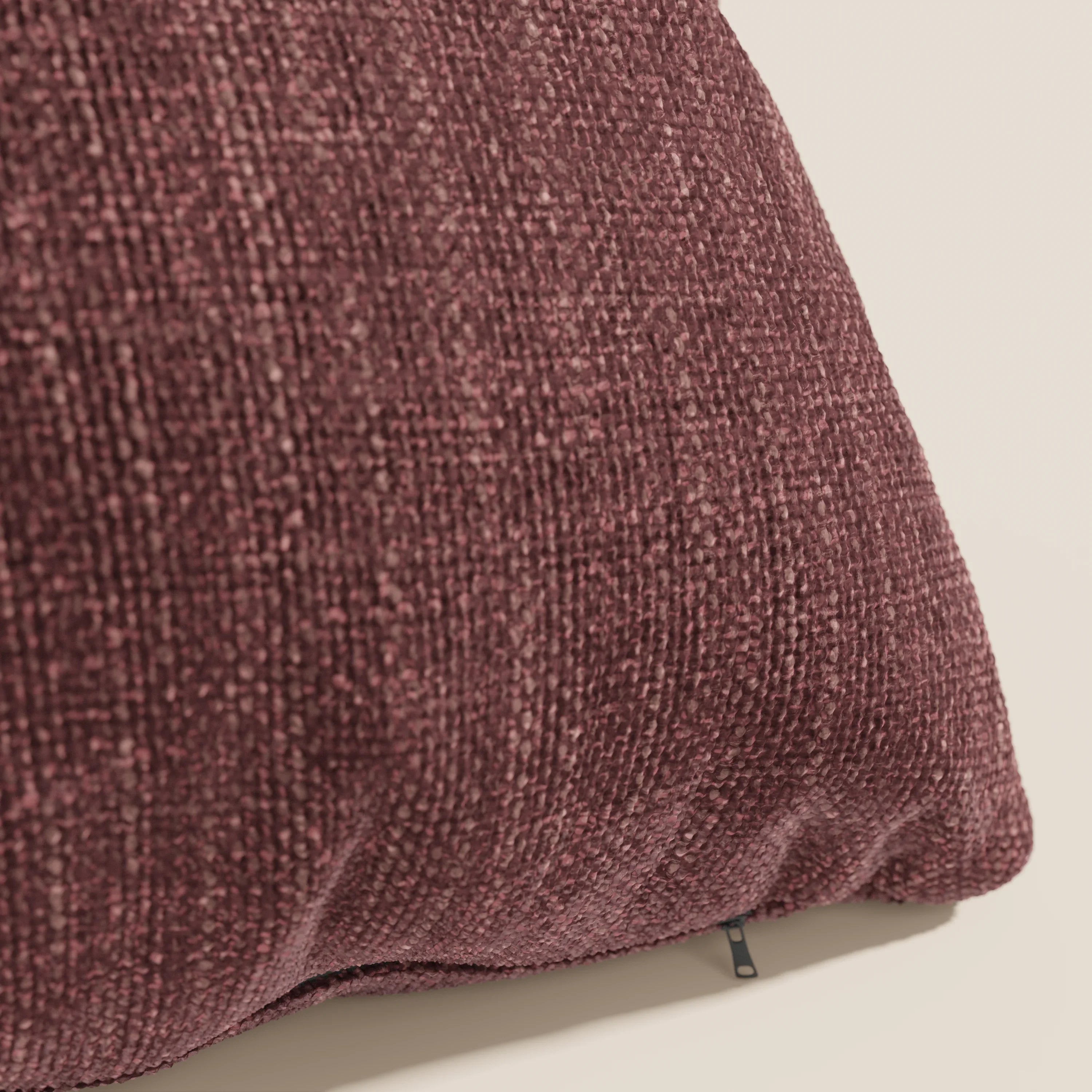 Primo piano del cuscino Divani.Store Lyon in T06 rosso: un cuscino decorativo di colore bordeaux intenso, realizzato in tessuto morbido, intrecciato e impermeabile, con una sottile lucentezza e fibre visibili. Una piccola etichetta nera sottolinea il bordo inferiore su uno sfondo beige chiaro.