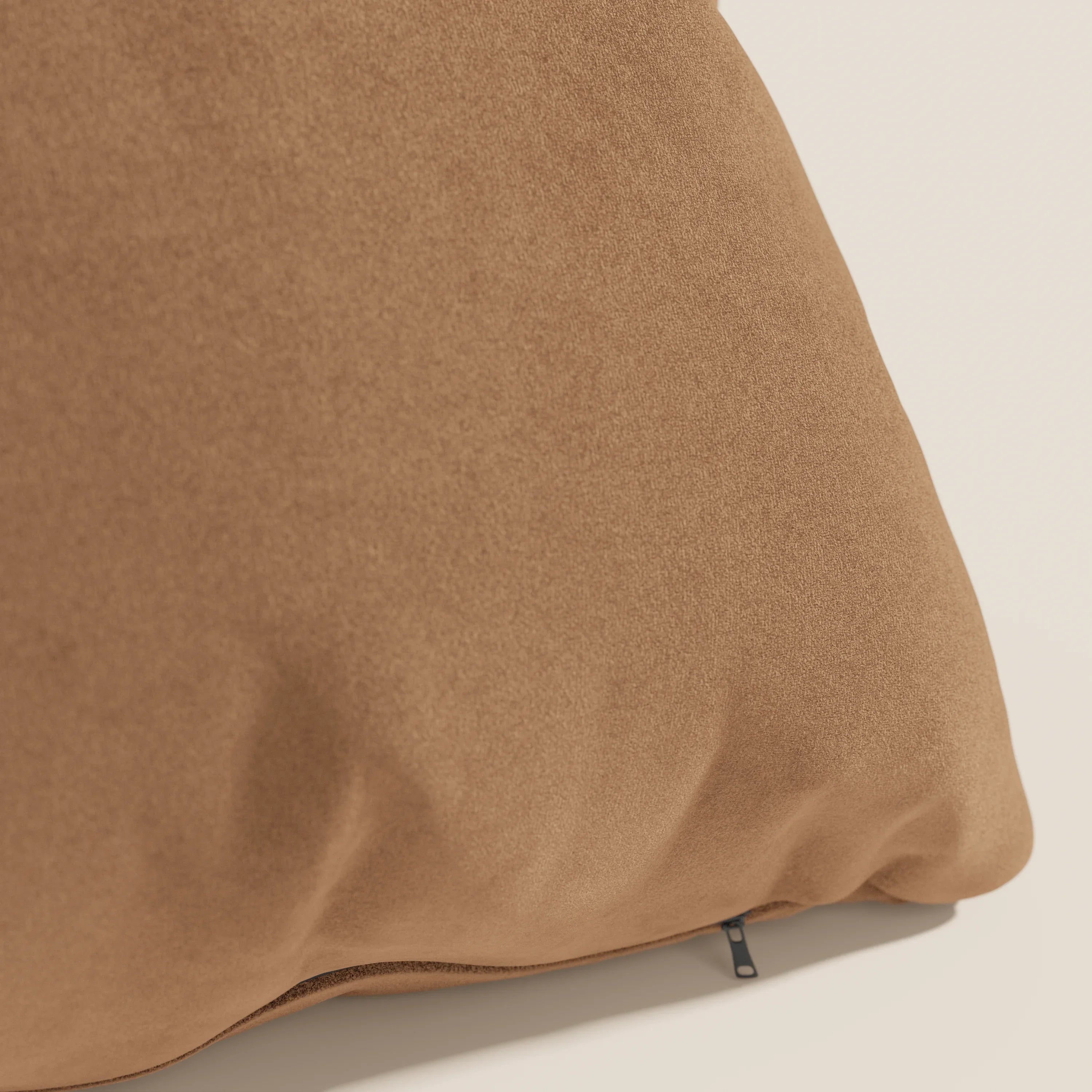 Primo piano del cuscino Jazz di Divani.Store in T11 cuoio, realizzato in microfibra tecnica antimacchia. Il cuscino, di grandi dimensioni e di colore marrone cammello, è caratterizzato da sottili pieghe e da una targhetta nera, esposta su una superficie chiara per un tocco di eleganza.