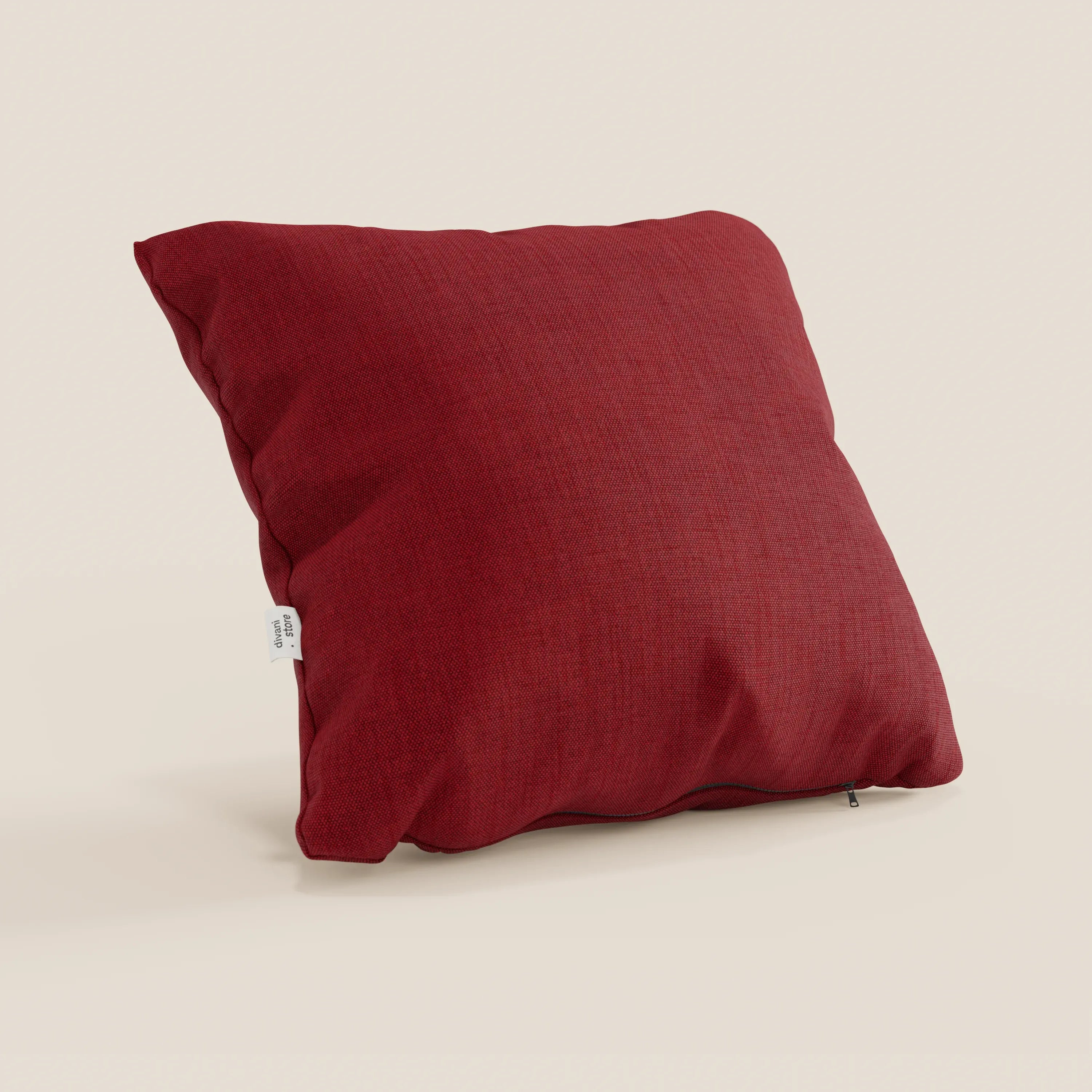 Un cuscino Honey di Divani.Store, 45x45 cm in T13 rosso simil cotone impermeabile, poggia su una superficie beige. Presenta un sottile rivestimento effetto cotone, una piccola etichetta bianca sul lato e una cerniera lungo il bordo inferiore.
