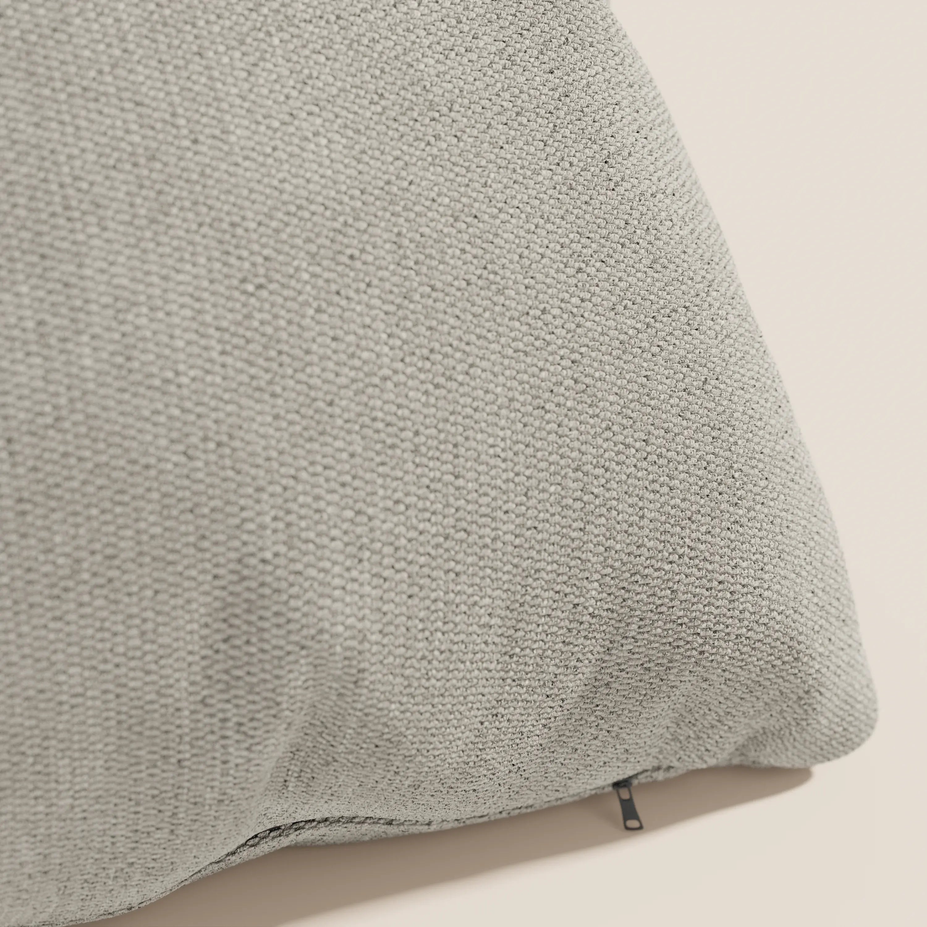 Primo piano del cuscino Miami 45x45 in tessuto impermeabile T14 tortora di Divani.Store, che mostra la trama intrecciata e una piccola cerniera nera nella cucitura in basso a destra, su uno sfondo chiaro.