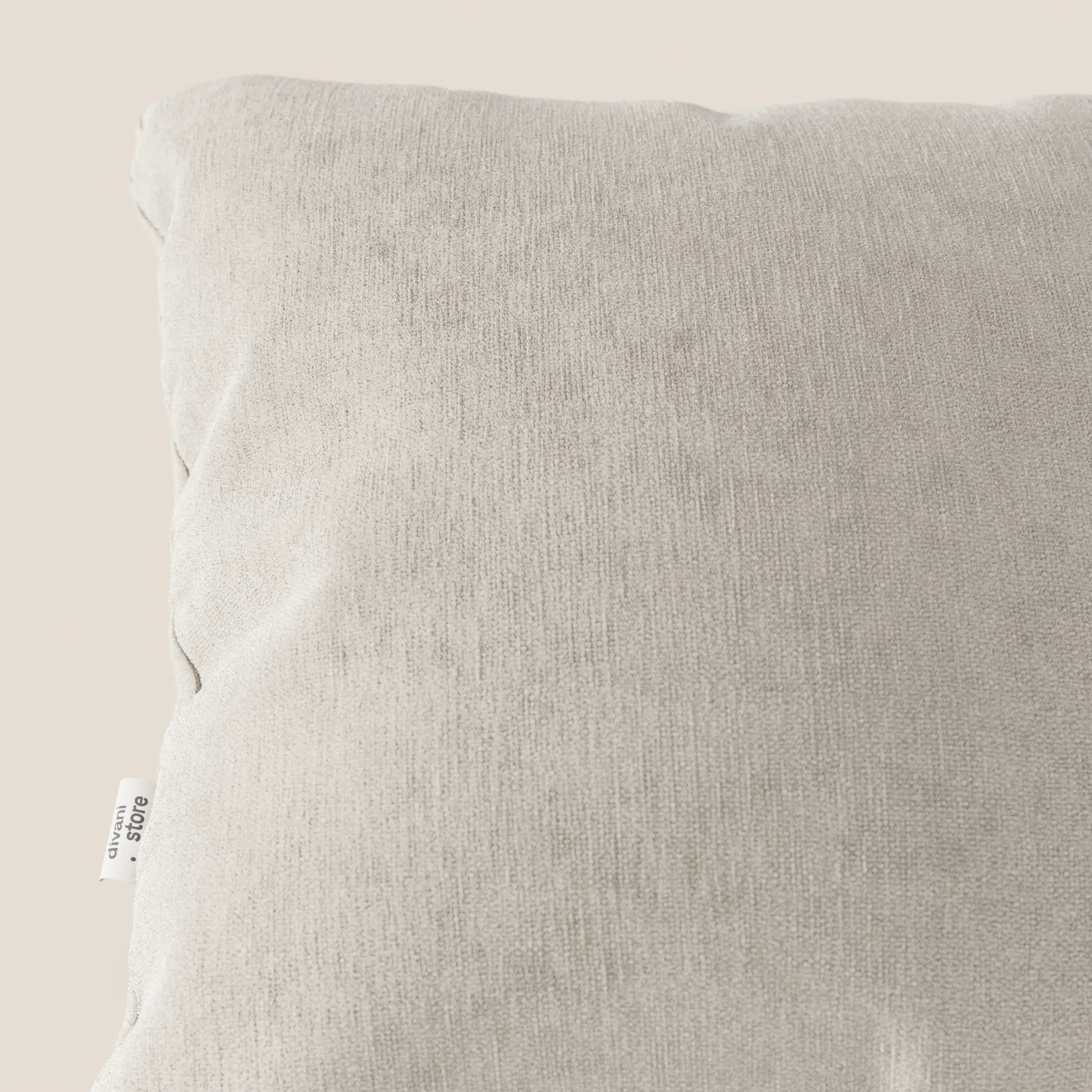 Primo piano del cuscino Bolero di Divani.Store in grigio chiaro, con una piccola etichetta bianca sulla cucitura sinistra. Realizzato in morbido tessuto T31 antimacchia, impermeabile e non restringente. Su uno sfondo beige neutro.