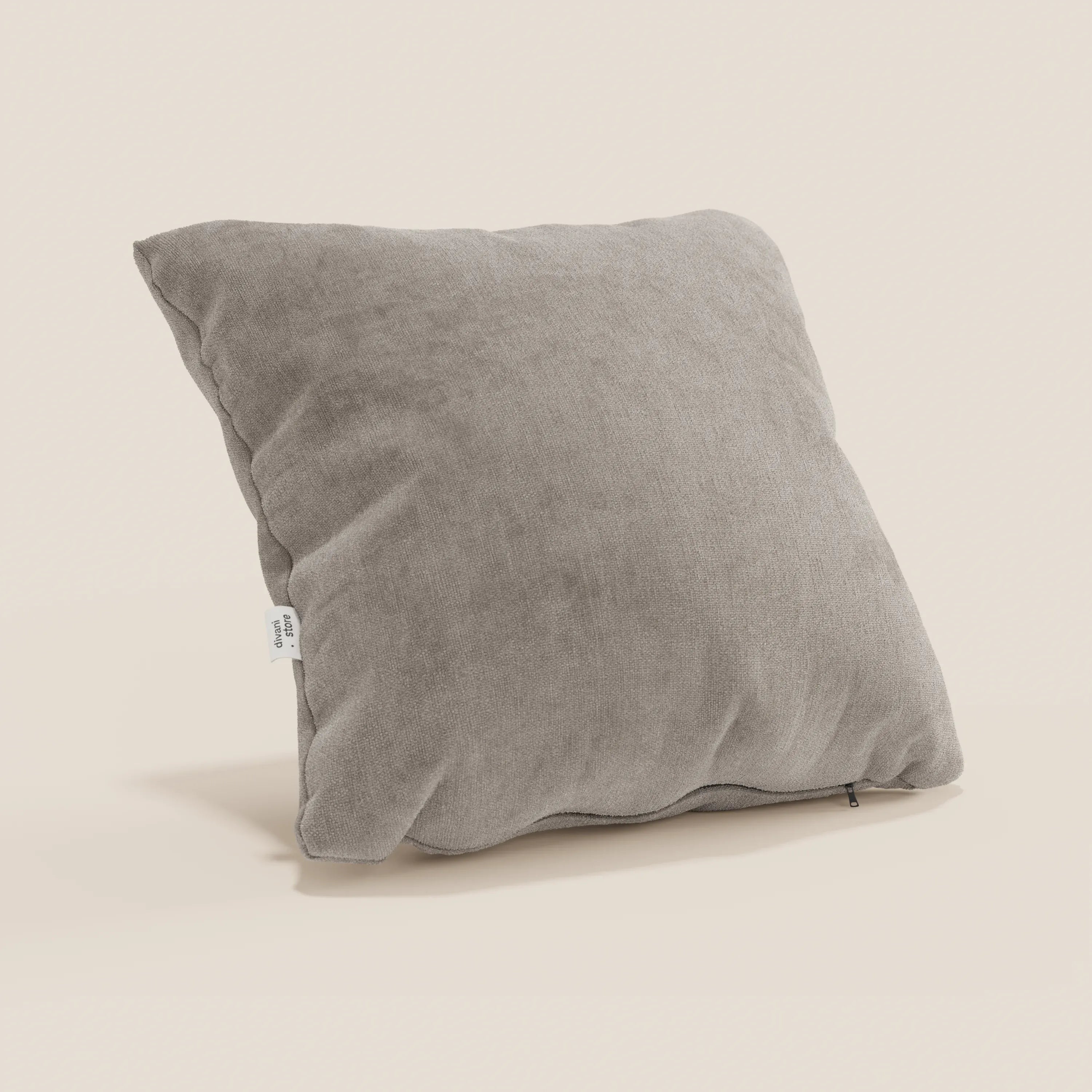 Il cuscino Bolero di Divani.Store, di colore grigio chiaro con forma quadrata e tessuto T31 morbido e strutturato, è caratterizzato da un'etichetta bianca sulla cucitura sinistra e da una cerniera sul fondo. Fotografato su uno sfondo beige chiaro.