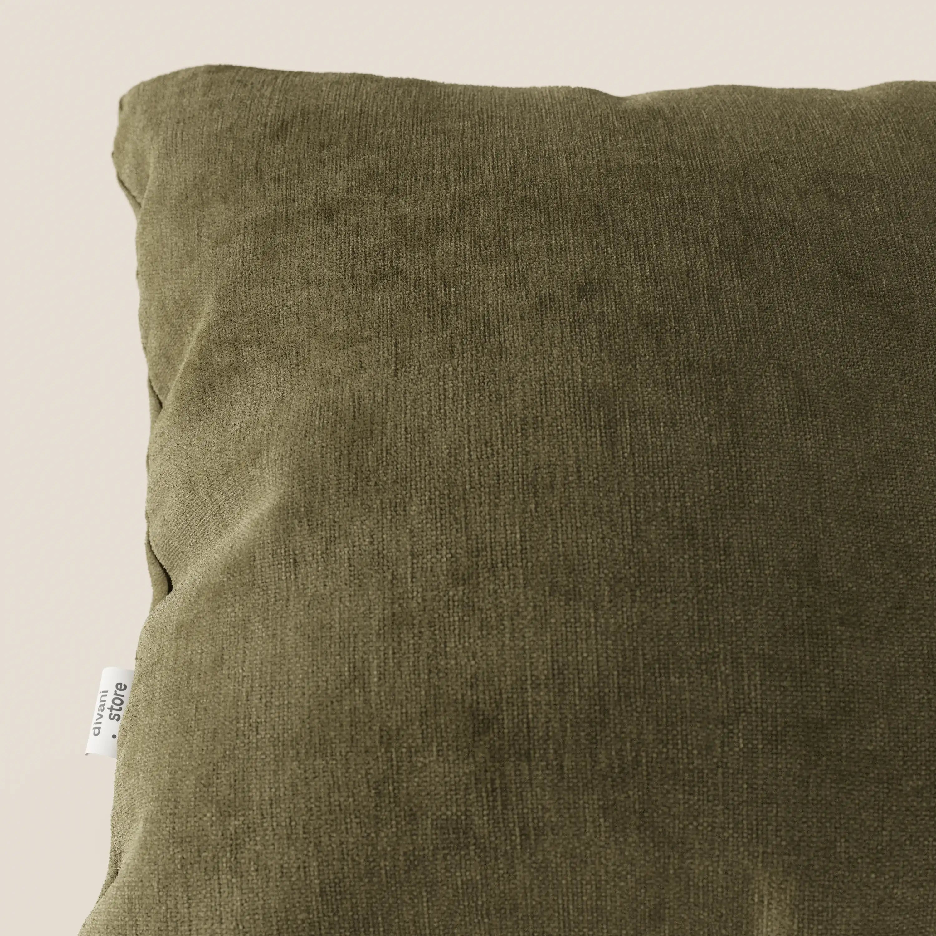 Primo piano di un cuscino Bolero quadrato verde oliva di Divani.Store in morbido tessuto T31, resistente alle macchie, impermeabile e non restringente, con una sottile trama a coste; piccola etichetta laterale bianca, su sfondo beige chiaro.