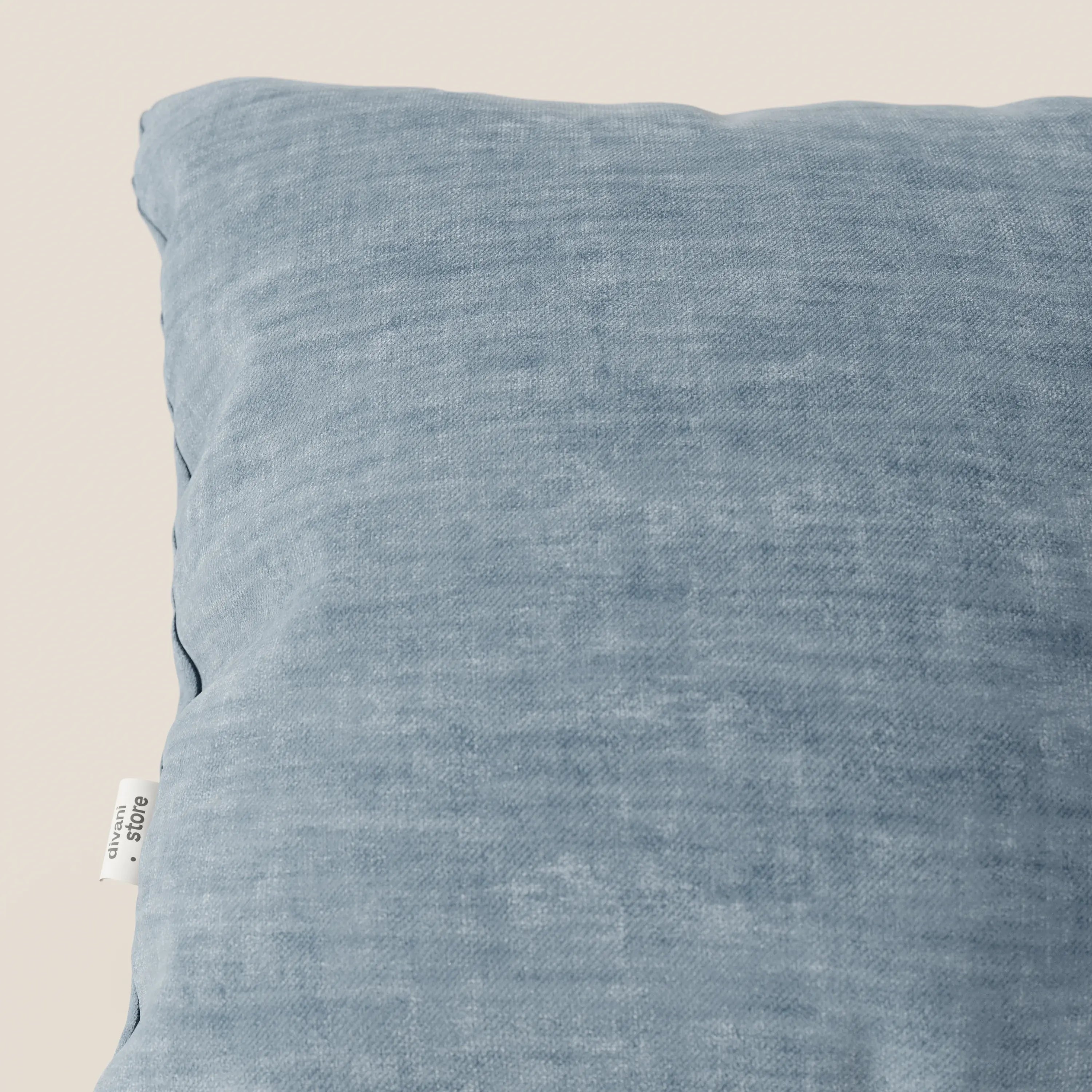 Primo piano del cuscino Sofia di Divani.Store, in velluto nuvolato azzurro. Il tessuto Easy Clean T35, morbido, antimacchia e impermeabile, presenta un'etichetta laterale con il marchio. Lo sfondo è semplice e neutro.