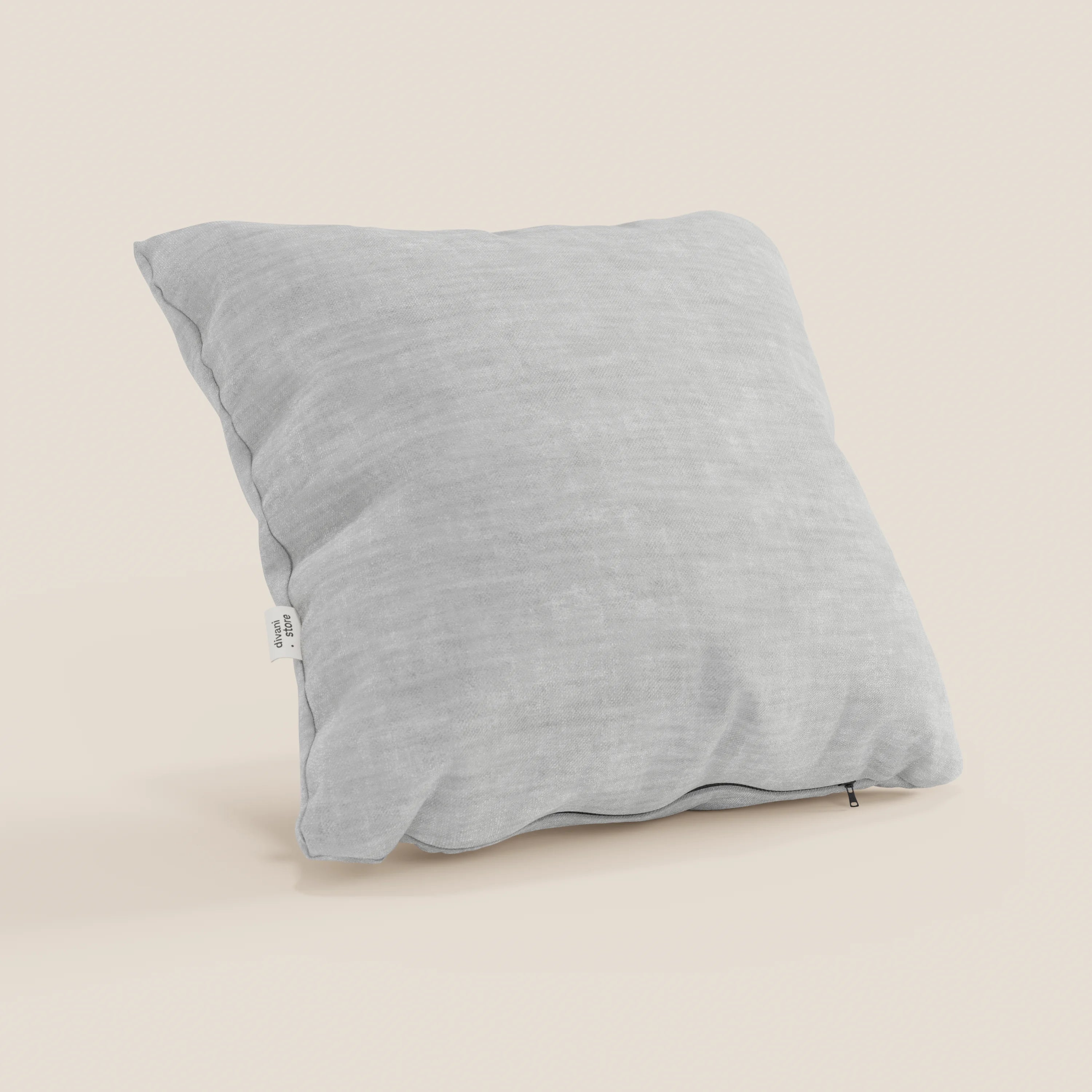 Il cuscino Sofia di Divani.Store, di forma quadrata e di colore grigio chiaro, è realizzato in morbido velluto nuvolato impermeabile e antimacchia e poggia su una superficie beige chiaro. Sul bordo sono visibili una piccola etichetta bianca e un discreto tiretto per la cerniera.
