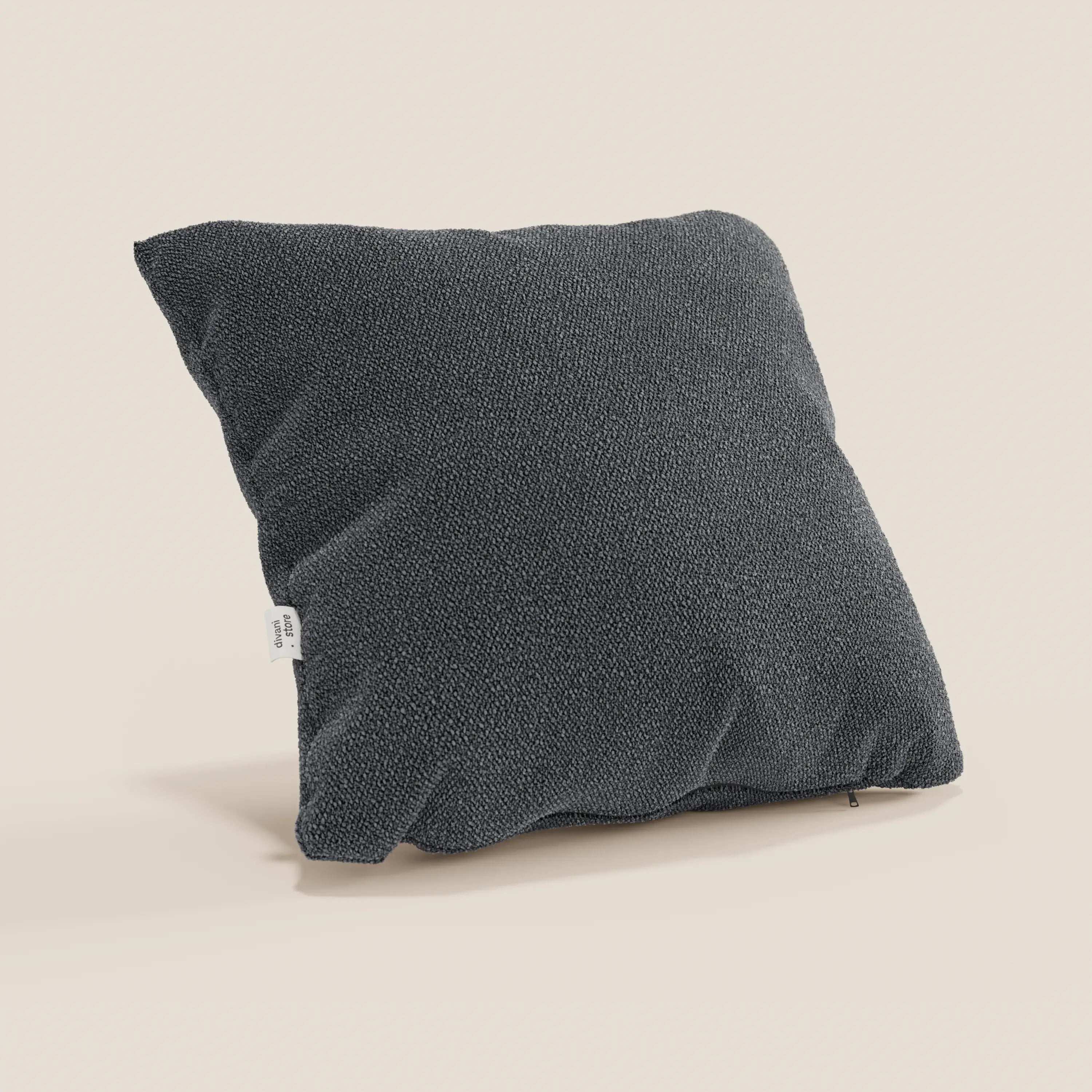 Un cuscino Lambada grigio scuro di Divani.Store, realizzato in tessuto fresco, antimacchia e impermeabile tipo cotone T33, con una piccola etichetta bianca su un lato, poggia morbidamente su una superficie beige chiaro su uno sfondo neutro.