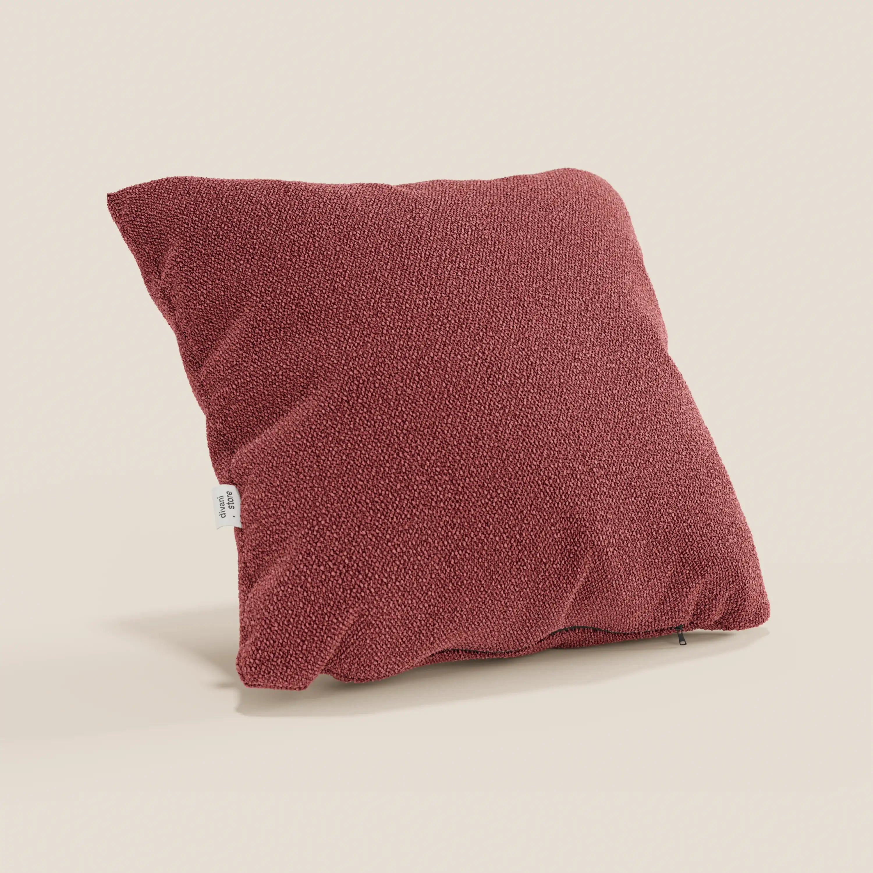 Un cuscino Lambada rosso quadrato di Divani.Store, realizzato in tessuto naturale simil-cotone T33 lavabile e impermeabile, sta in piedi su uno sfondo beige chiaro con una piccola etichetta bianca su un lato.