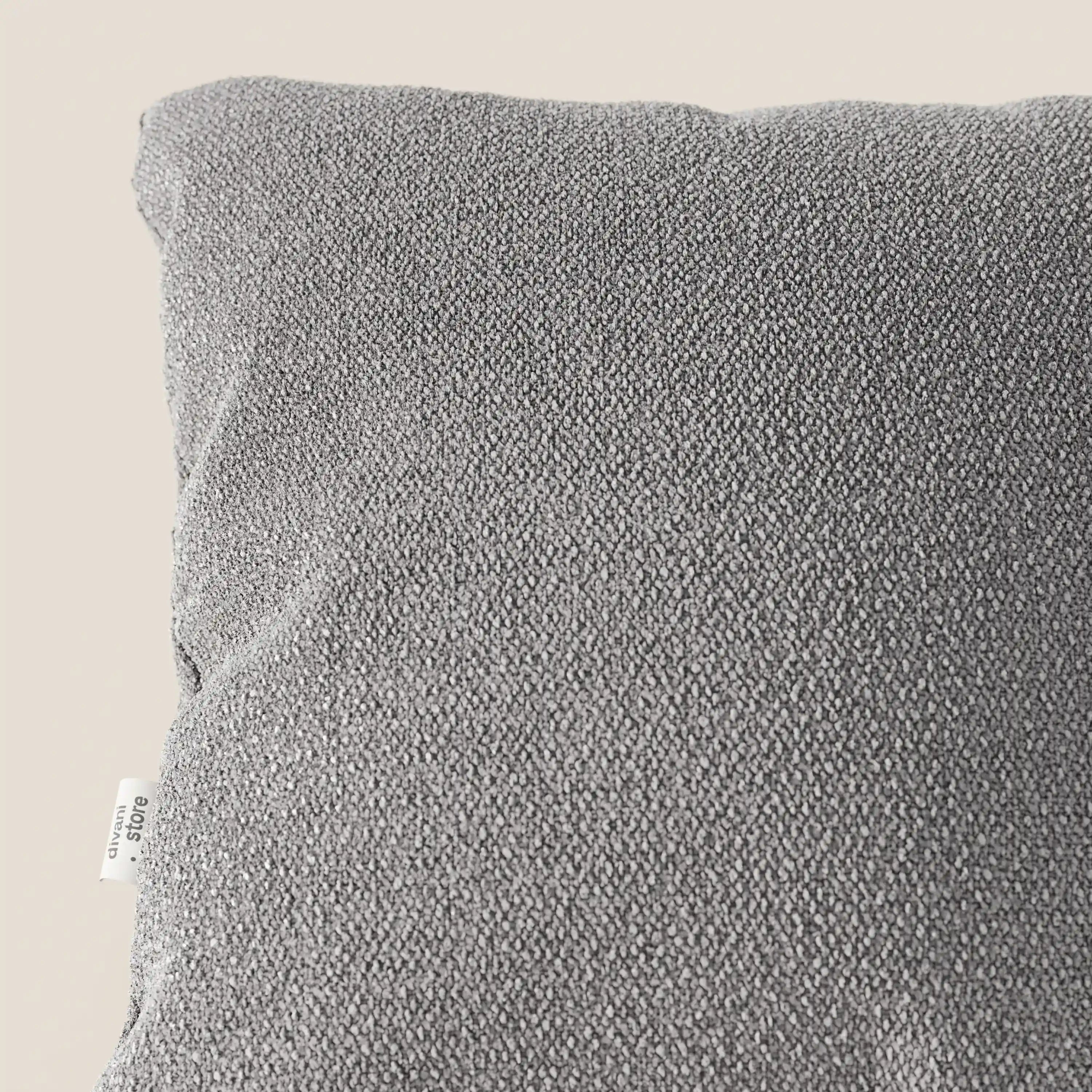 Primo piano dell'angolo superiore di un cuscino Lambada grigio di Divani.Store, realizzato con un tessuto T33 fresco e naturale simile al cotone, resistente alle macchie e all'acqua. Una piccola etichetta bianca con testo appare sulla cucitura laterale vicino all'angolo.