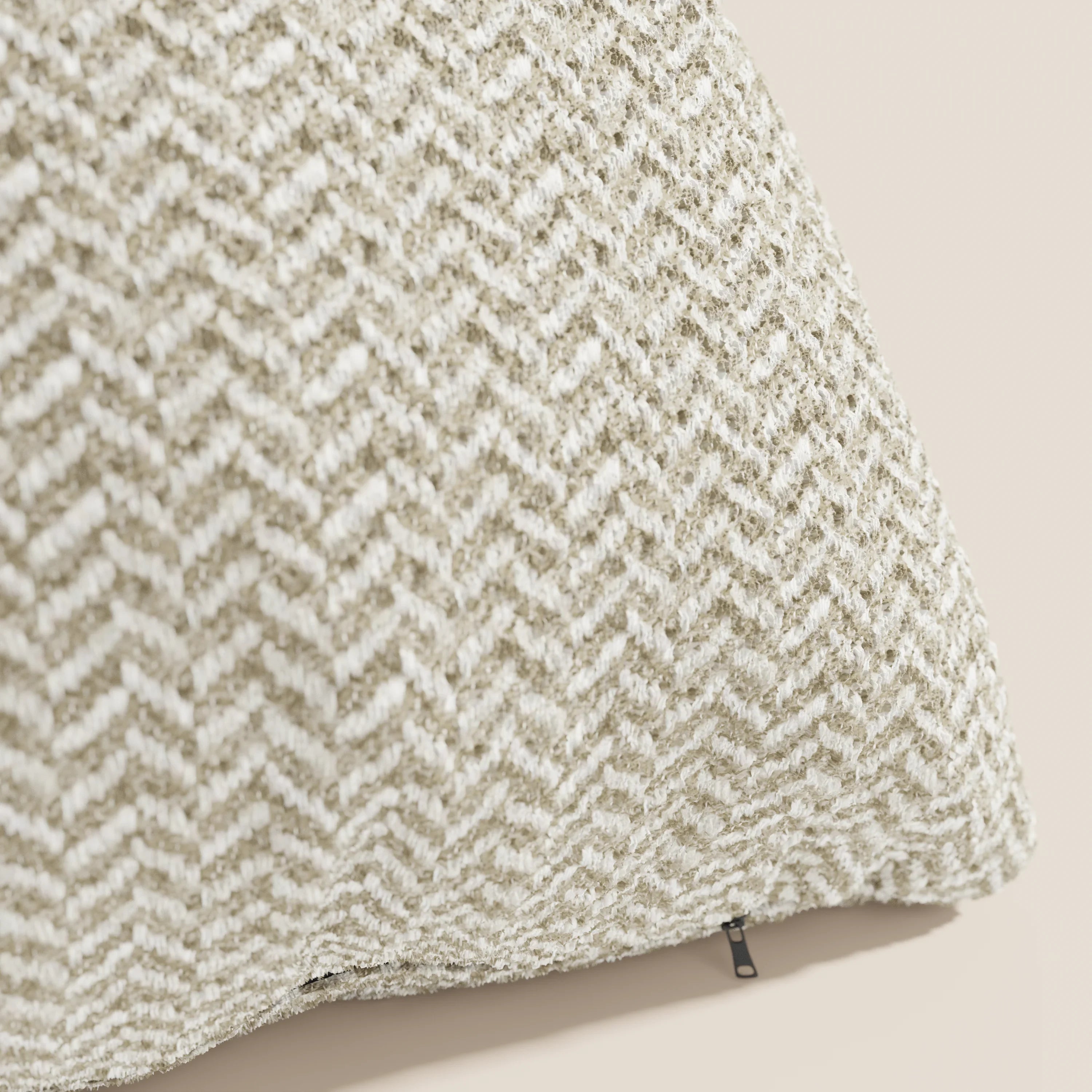 Un primo piano del modello "Sorrento Cuscino 45x45 in Lino" di Divani.Store mette in risalto la sua trama a spina di pesce nei toni del beige e del bianco, i delicati dettagli intrecciati e un piccolo tirazip nero su uno sfondo beige chiaro a tinta unita.