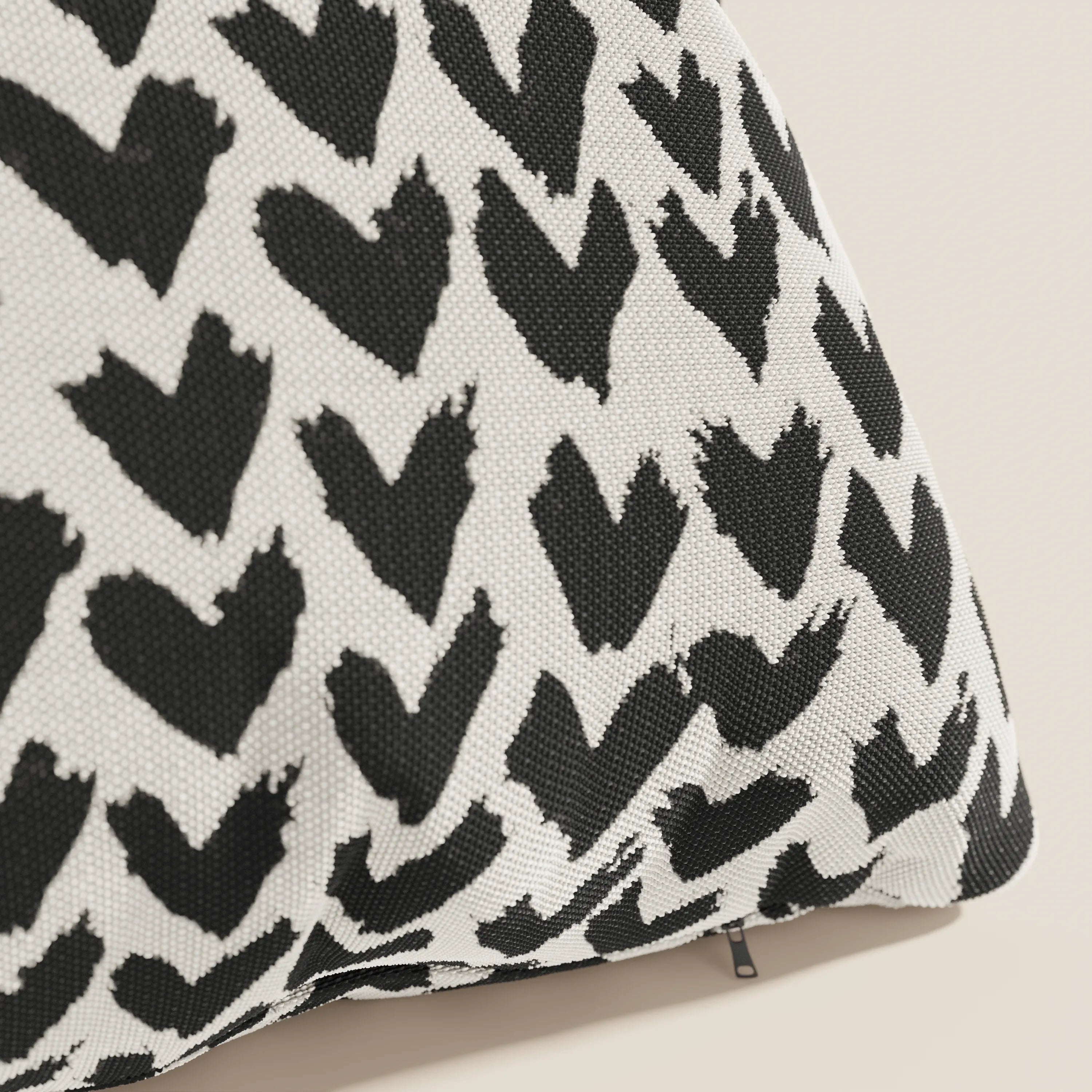 Primo piano dei cuscini geometrici Arrow di Divani.Store, caratterizzati da un tessuto idrorepellente nero con motivo a cuori irregolari e una piccola cerniera in basso a destra su sfondo chiaro.