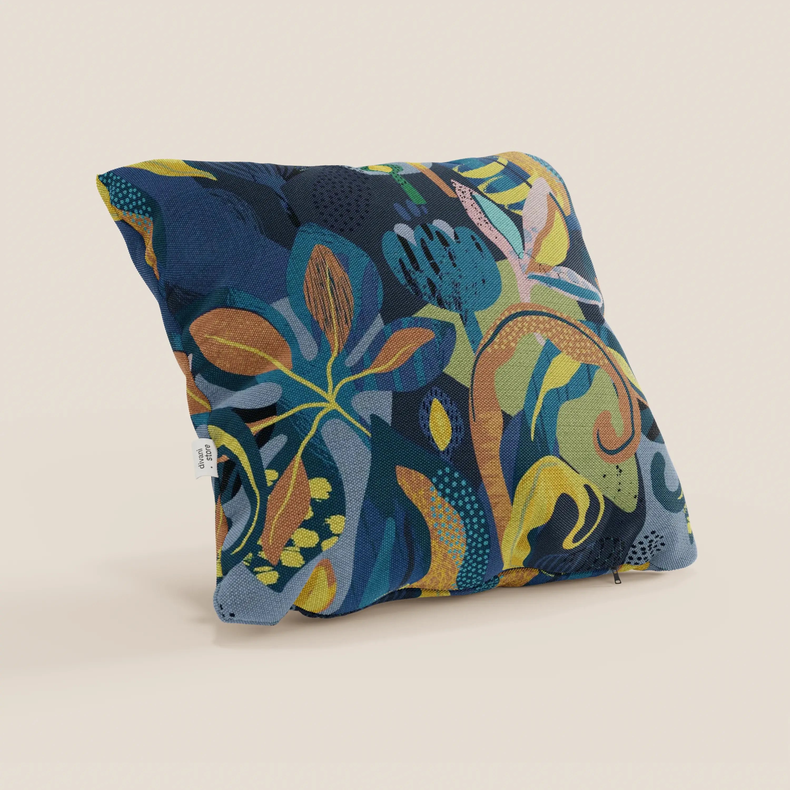 Il cuscino Joy collezione di Divani.Store presenta un disegno botanico multicolore con foglie astratte in blu, verde, arancione e giallo su un tessuto impermeabile di cotone fresco, raffigurato su uno sfondo beige con una piccola etichetta bianca.
