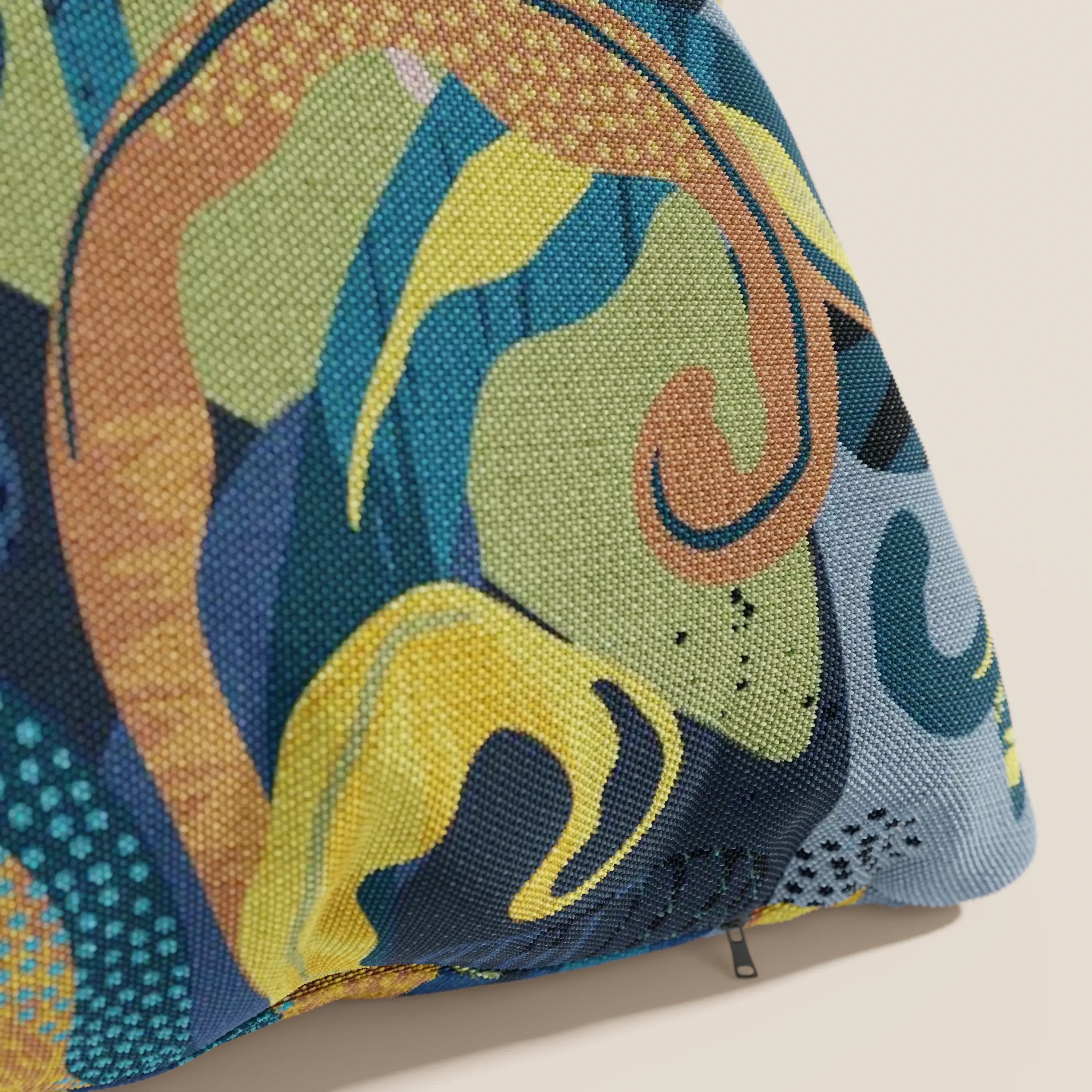 Un primo piano di Joy collezione cuscini a fantasie multicolor di Divani.Store in fresco cotone impermeabile blu mostra un tessuto strutturato con motivi astratti blu, verdi, gialli, marroni e verde acqua. In basso a destra compare una piccola cerniera.