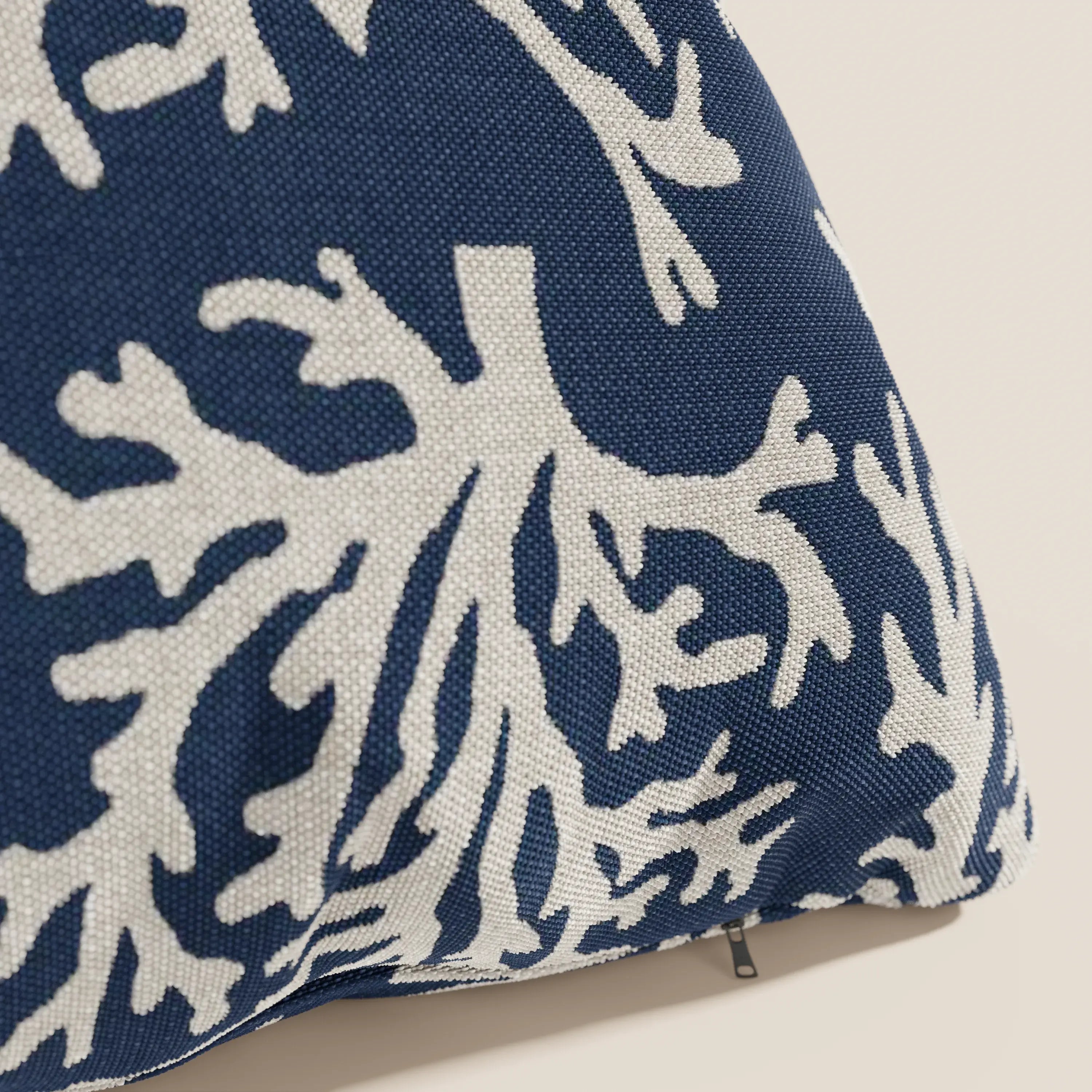 Primo piano di un cuscino Nautilus di Divani.Store in tessuto impermeabile blu con motivo di barriera corallina bianca, che mostra una texture visibile e una cerniera aperta sul bordo. Sfondo chiaro a tinta unita.
