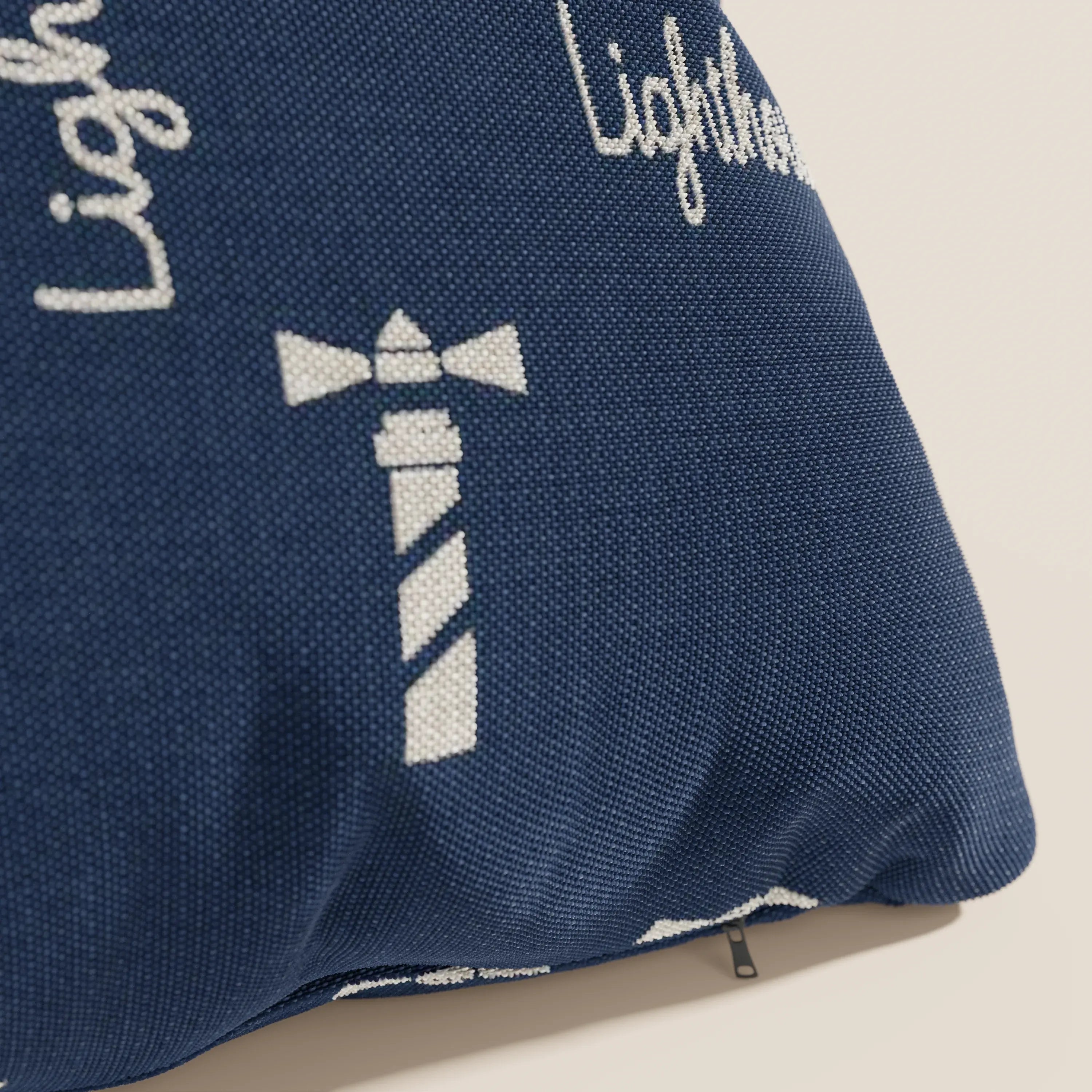 Primo piano di un cuscino Nautilus blu navy di Divani.Store, con grafica a strisce bianche e scritta "Lighthouse". Realizzato in tessuto impermeabile con cucitura angolare a vista e piccola cerniera in basso a destra.