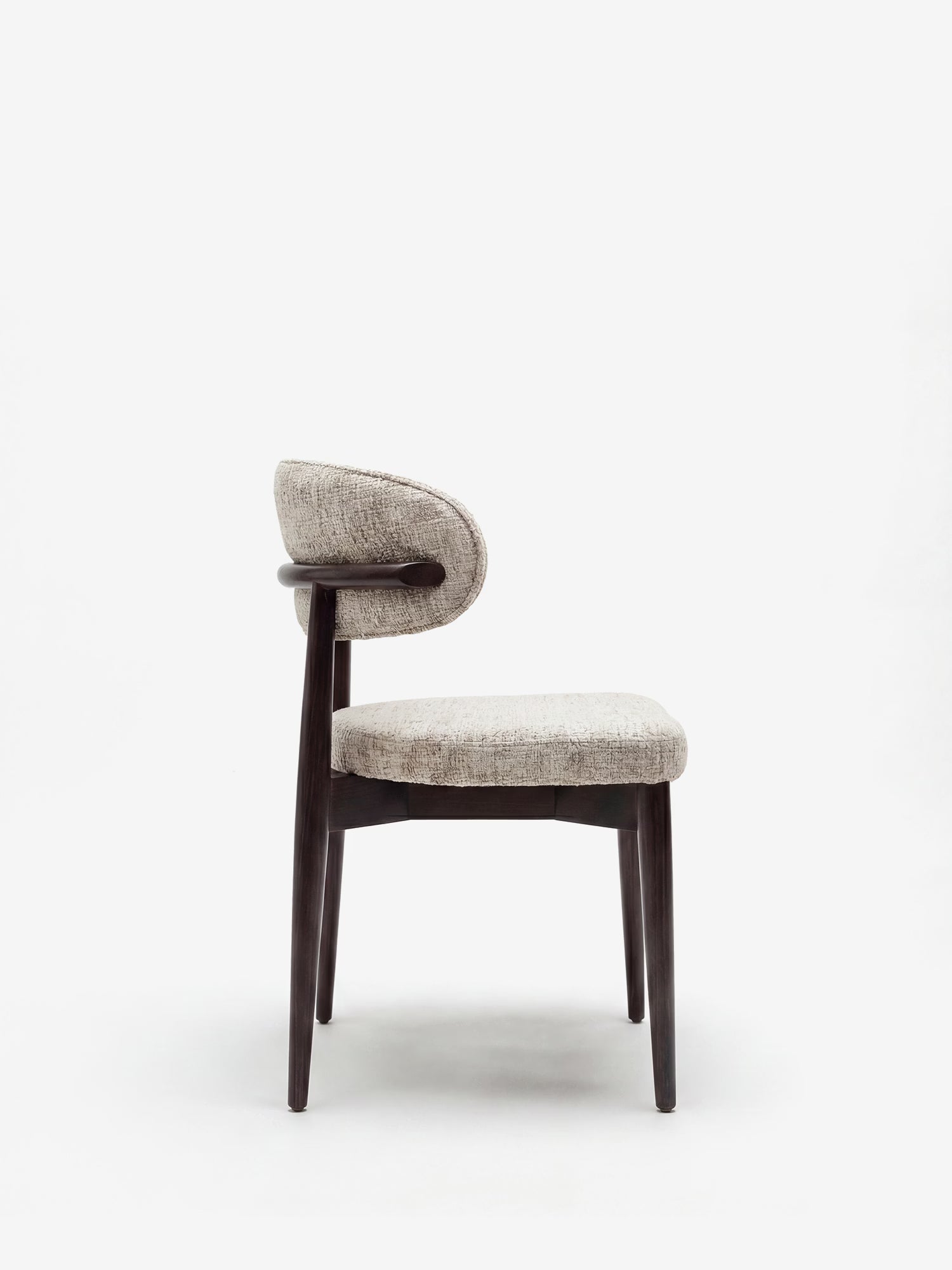 La sedia di design imbottita Dafne di Divani.Store presenta una struttura in legno massello wengé scuro e quattro gambe angolate, con rivestimento in ciniglia chiara certificata OEKO-TEX® che ricopre la seduta e lo schienale curvi, raffigurata di profilo su sfondo bianco.