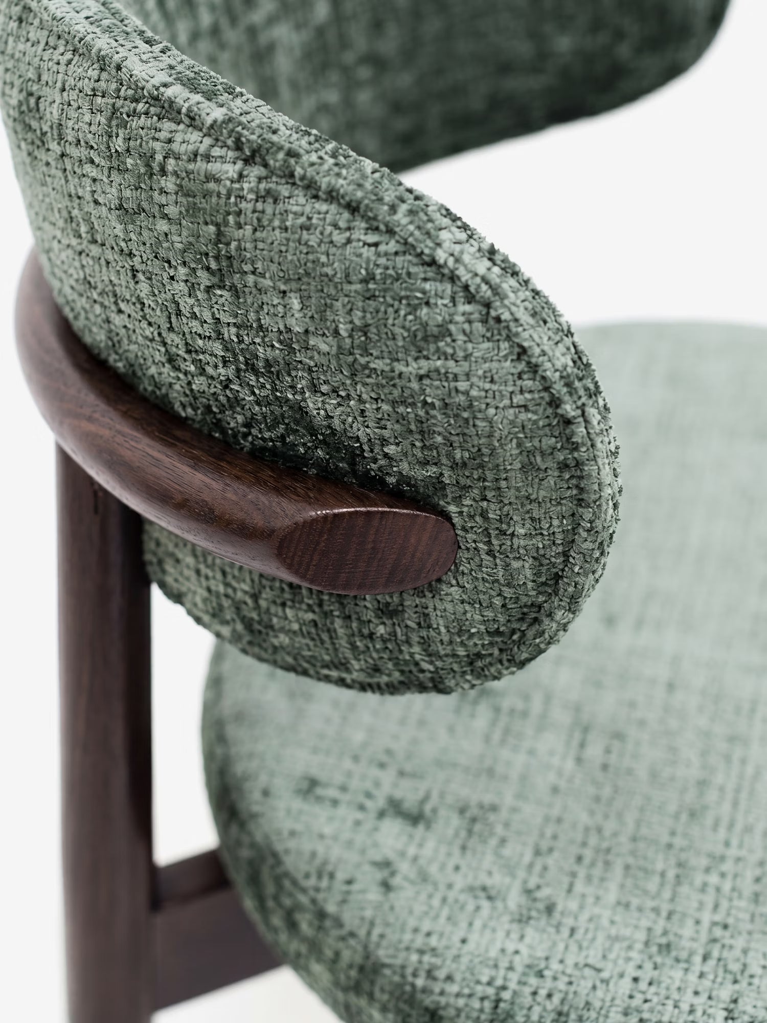 Primo piano della sedia Dafne di Divani.Store: una sedia contemporanea realizzata in ciniglia ecologica certificata OEKO-TEX®, con schienale e seduta imbottiti di forma arrotondata e un dettaglio curvo in legno massello di wengé, che risalta sullo sfondo bianco a tinta unita.