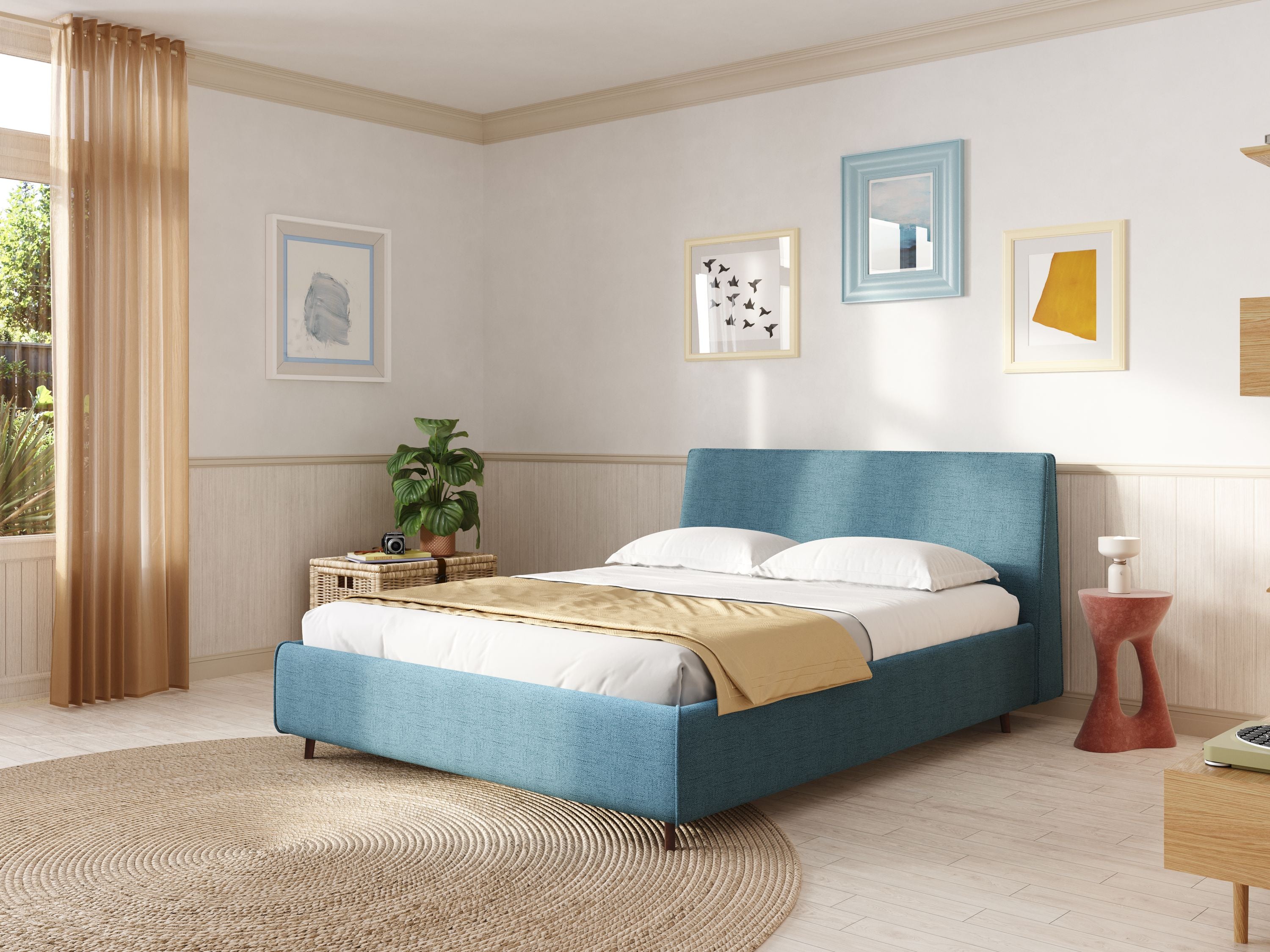 Una camera da letto illuminata dal sole è caratterizzata dal letto Letti.store Justin imbottito contenitore e sfoderabile in tessuto fiammato impermeabile T03 azzurro, dalla biancheria da letto bianca, da una coperta abbronzata, da opere d'arte sulle pareti bianche, da un tappeto circolare intrecciato, da una pianta sul comodino in vimini, da un tavolino rosso e da tende abbronzate.