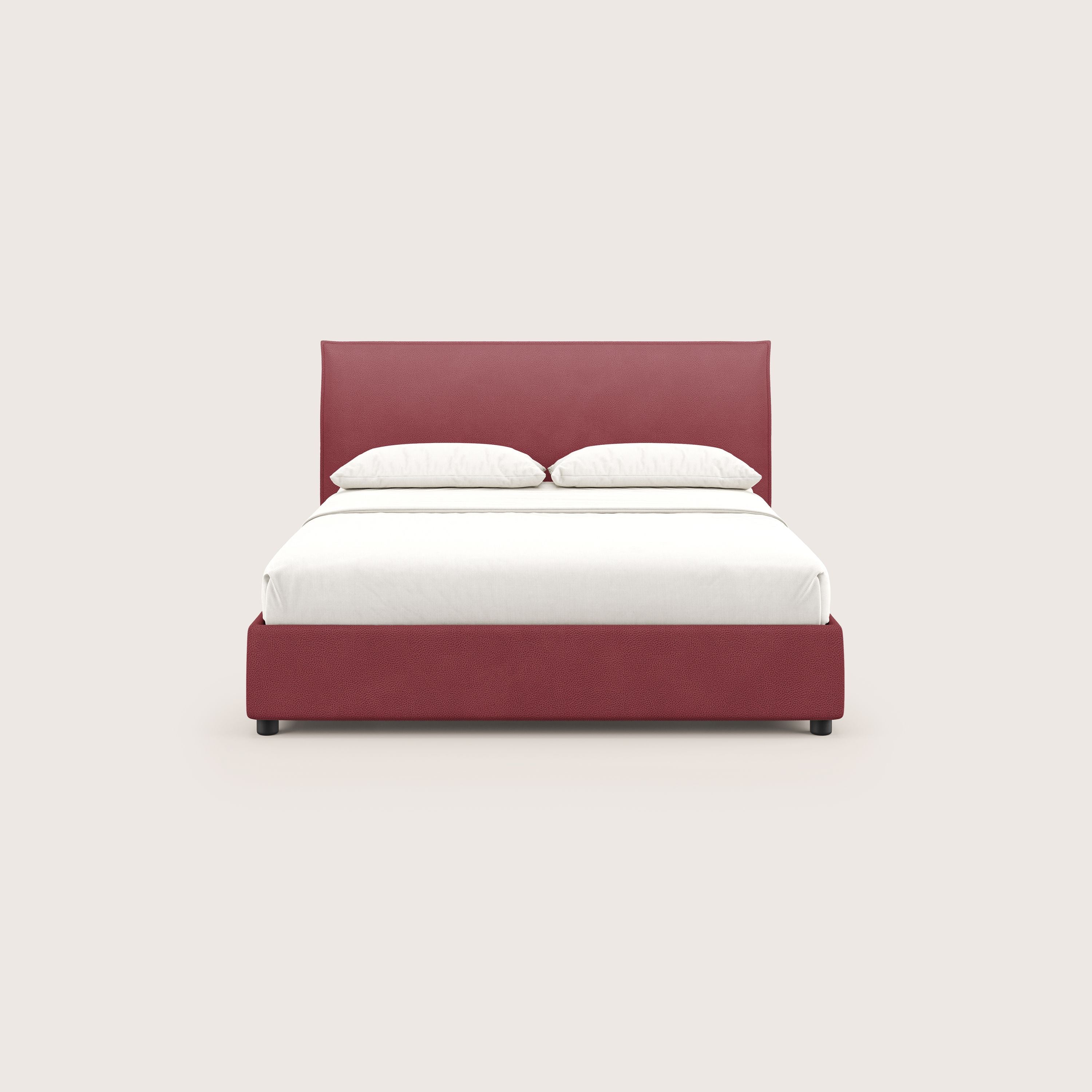 Il letto contenitore Nina di Letti.store è caratterizzato da un design minimal in microfibra rossa antimacchia effetto pelle, con una struttura e una testata imbottite, biancheria da letto bianca e due cuscini bianchi su uno sfondo beige chiaro.