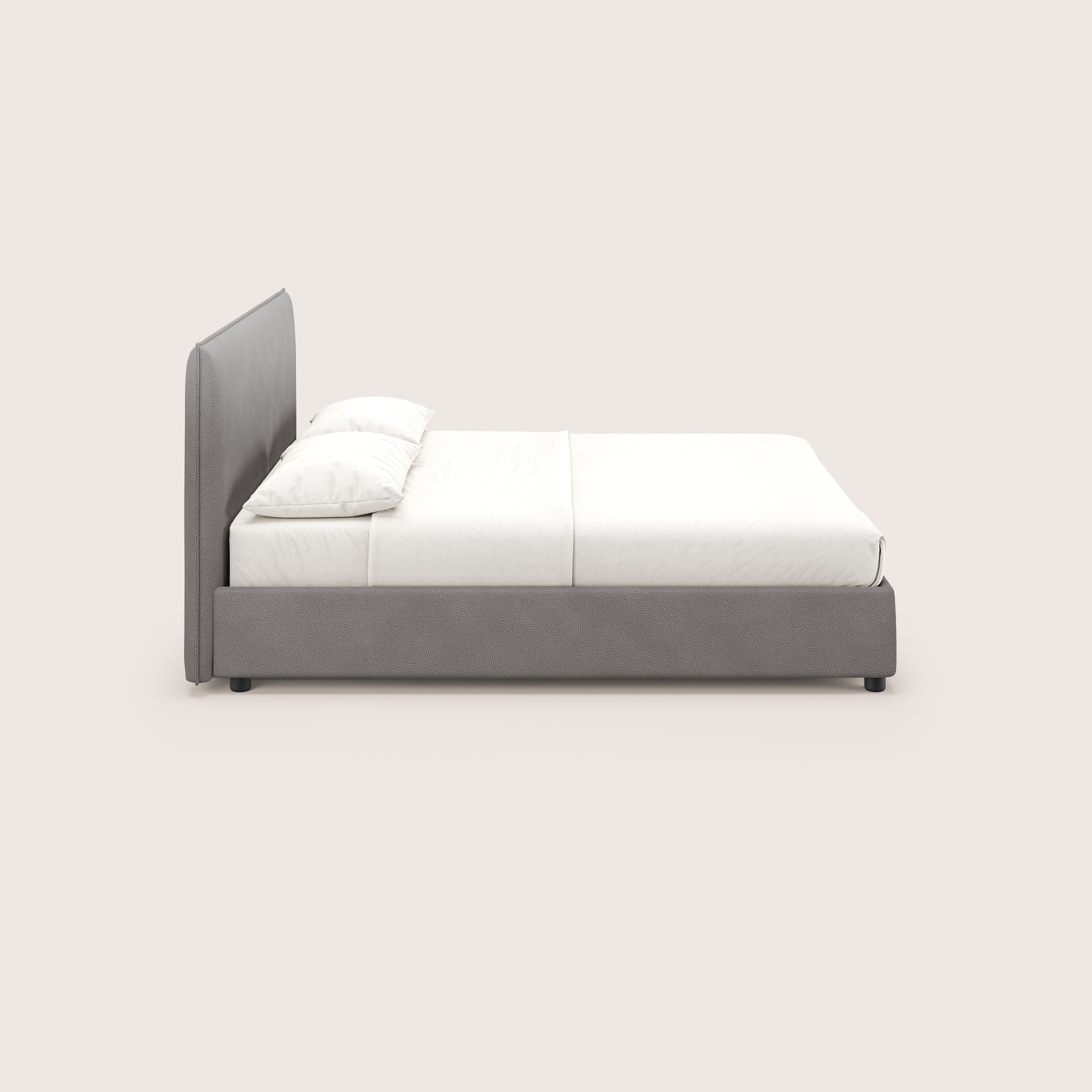 Una vista laterale di Nina letto contenitore di Letti.store mostra un'alta testiera in microfibra antracite, lenzuola bianche e una cornice bassa e minimale, che riflette il raffinato design italiano su uno sfondo chiaro.