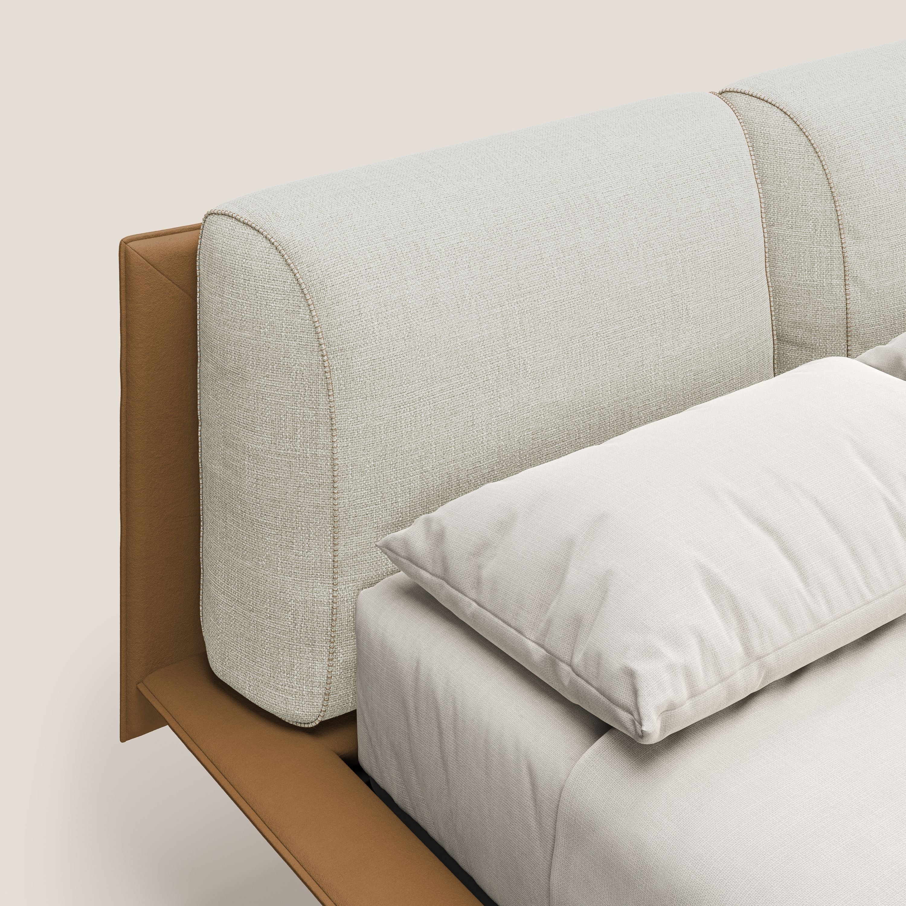 Primo piano di Petra letto di design bicolore di Letti.store, caratterizzato da cuscini in piuma, piedini in mogano e finitura impermeabile bicolore T11 e T06 cuoio-panna con biancheria da letto ordinata che ne evidenzia il design italiano.